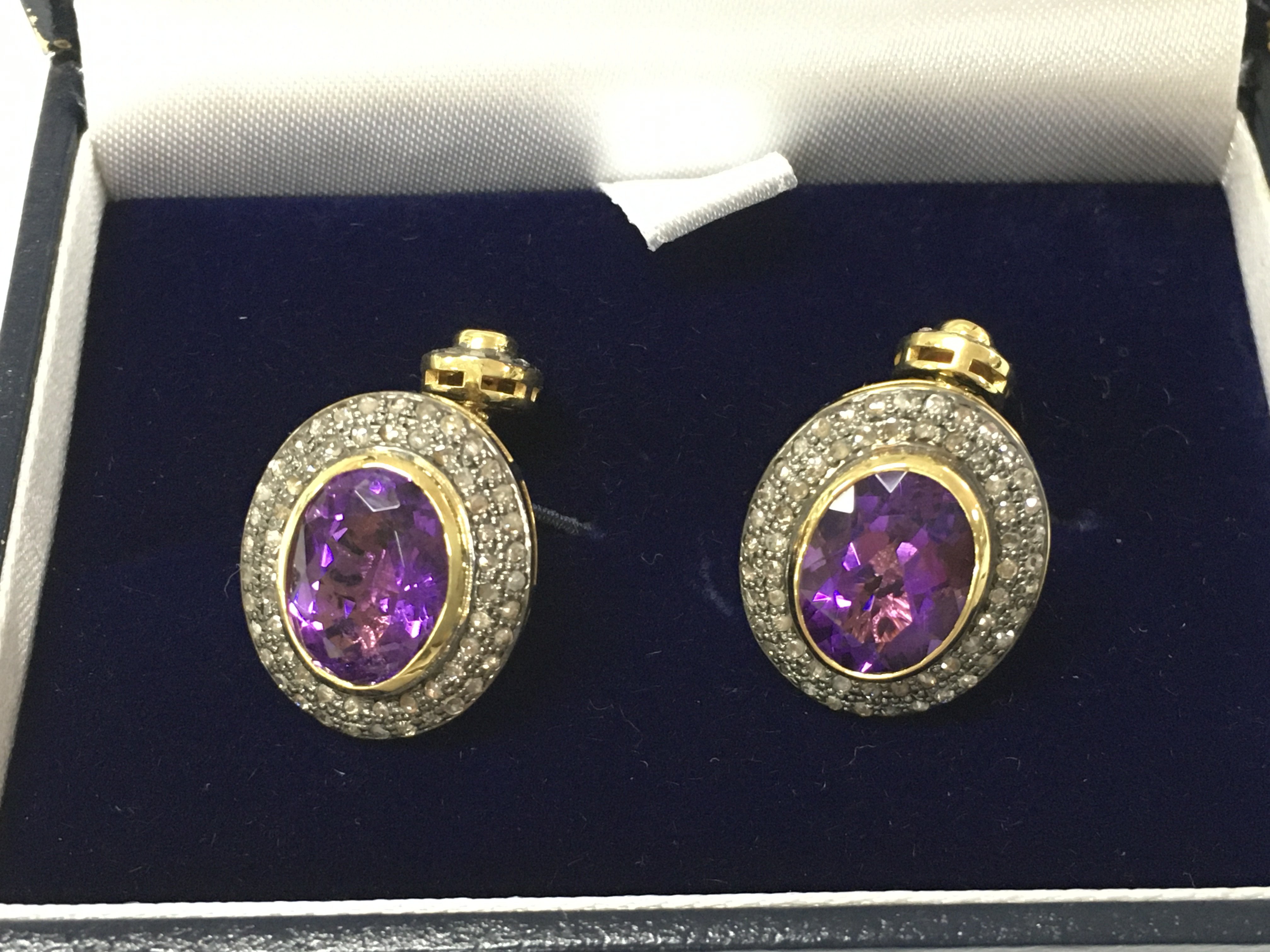 A pair of cufflinks in yellow metal set with oval amethyst surrounded by diamonds together with oval rubies surrounded by further diamonds. Amethyst 7.60ct Diamonds 1.15ct and rubies 0.40ct. Postage B