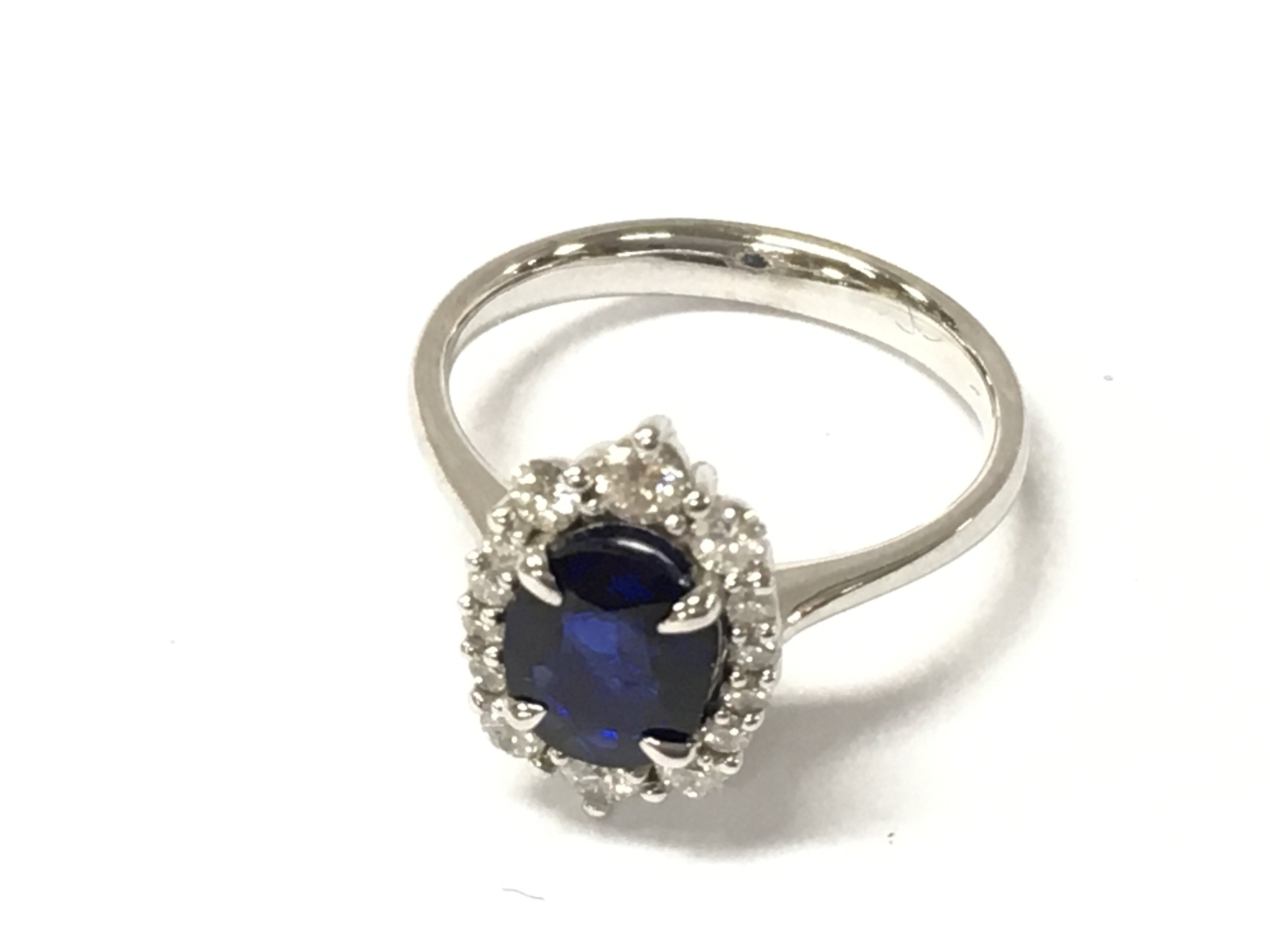 A 14ct white gold ring set with an oval sapphire and halo of graduated diamonds. Sapphire 1ct approx and diamonds 0.40ct Size M 1/2. Postage B