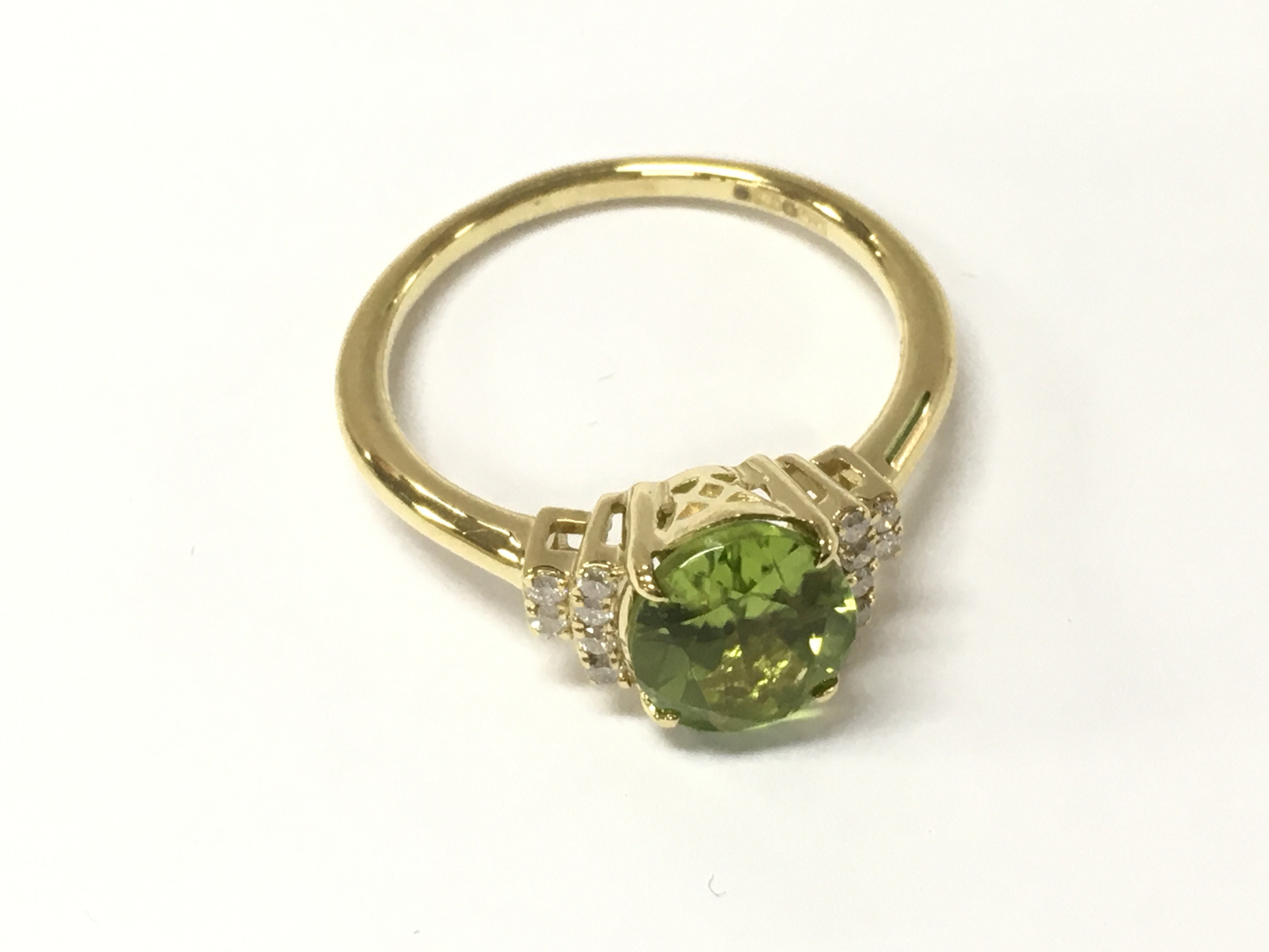 A 9ct gold ring set with an oval peridot flanked by diamonds in a terraced setting. Peridot 2.25ct and diamonds 0.11ct Approx. Size O