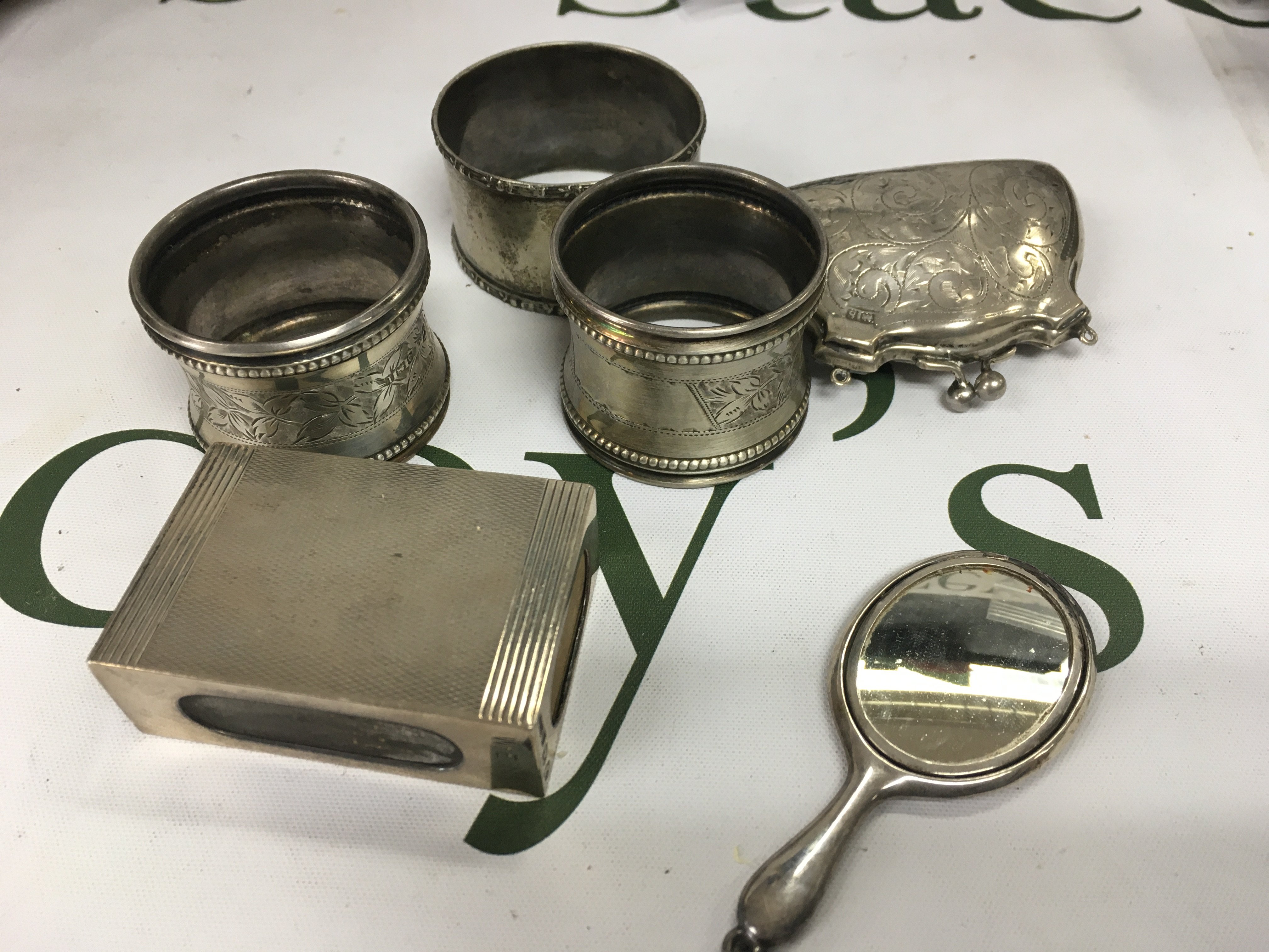 A small silver purse, silver napkin rings, a miniature mirror and a natch box case.