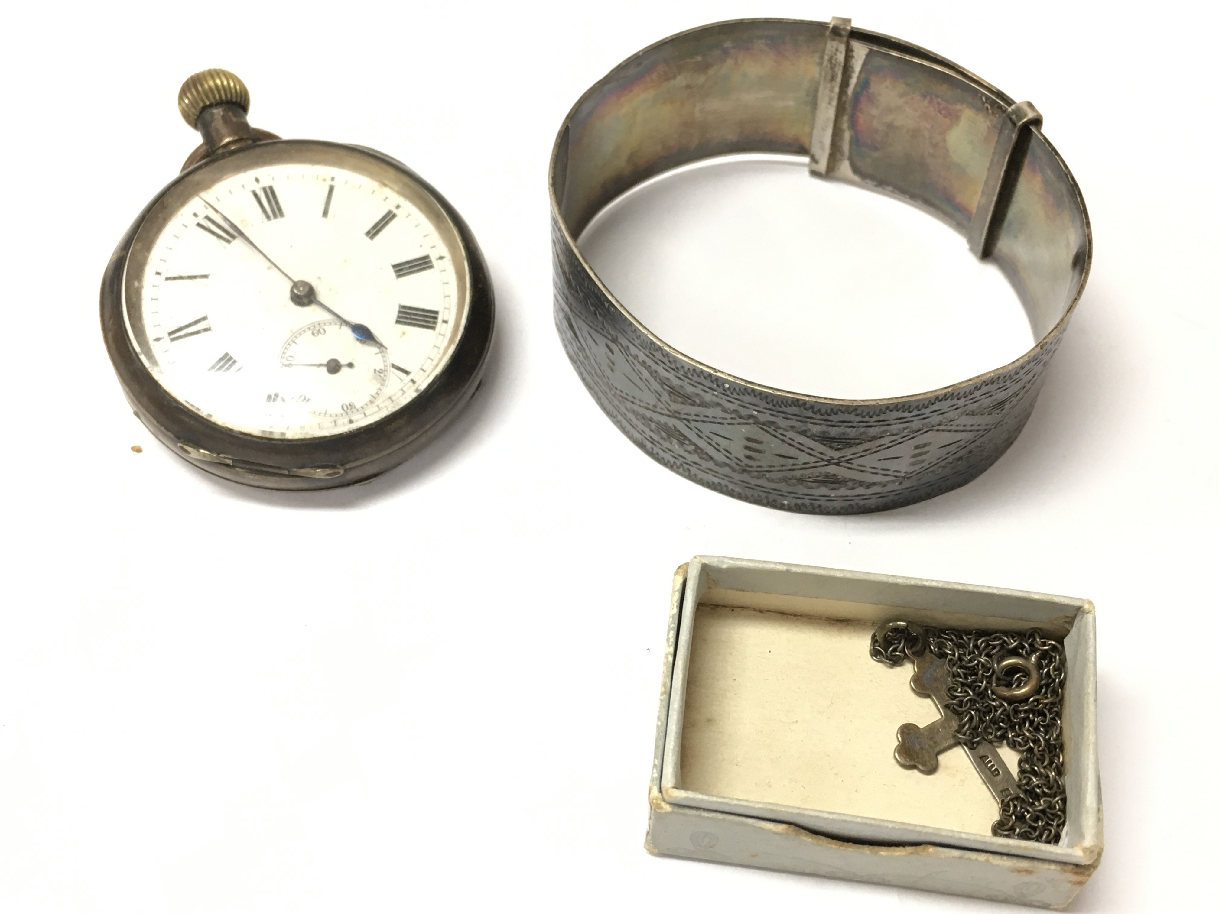 A silver cased pocket watch with a silver bangle and chain and cross pendant and a silver crest.