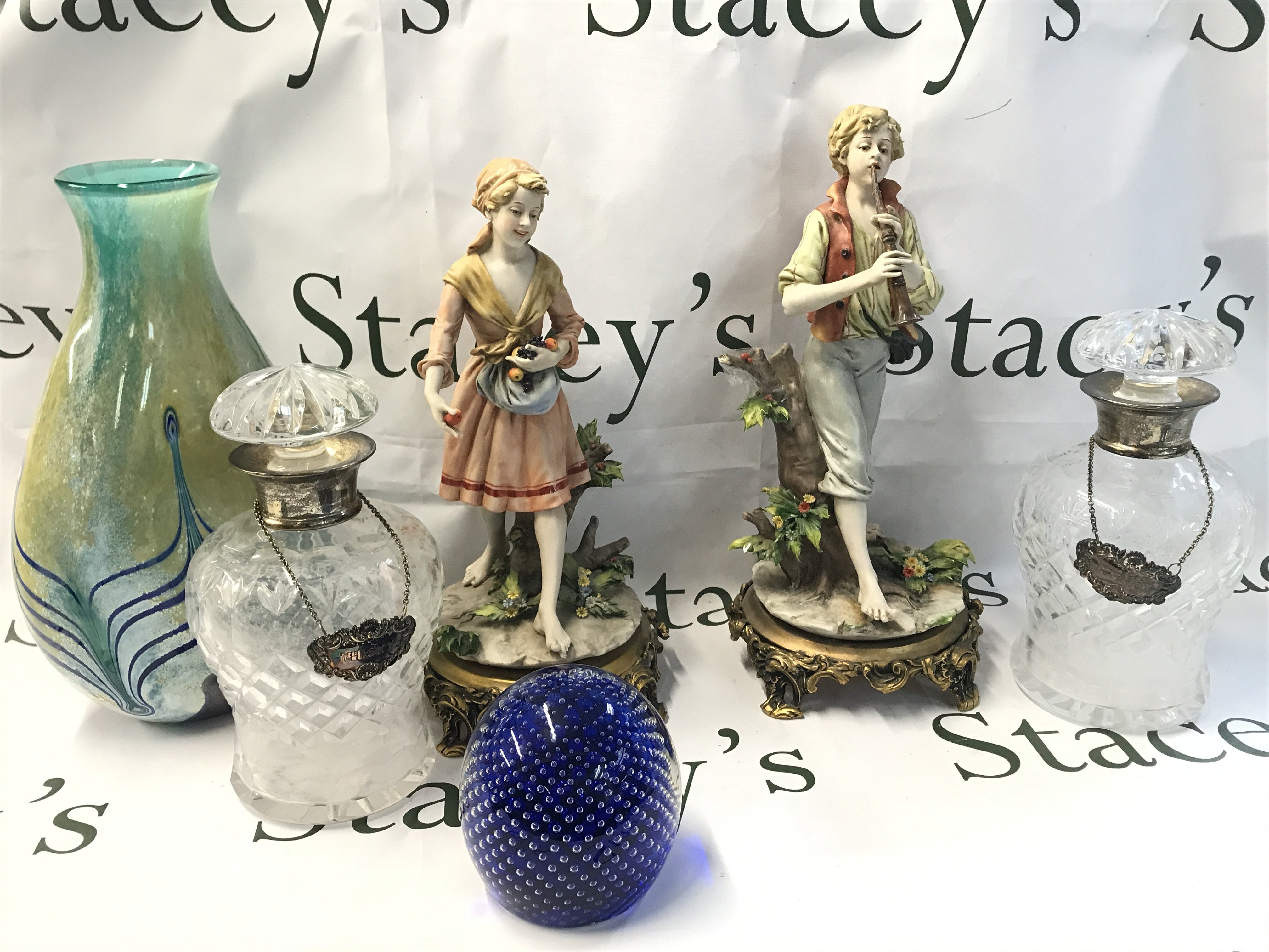 A pair of cut glass silver Hallmarked collared decanters with a pair of classical style Italian porcelain figures (one damaged) an art glass paper weight and a Caithness Khamsin vase