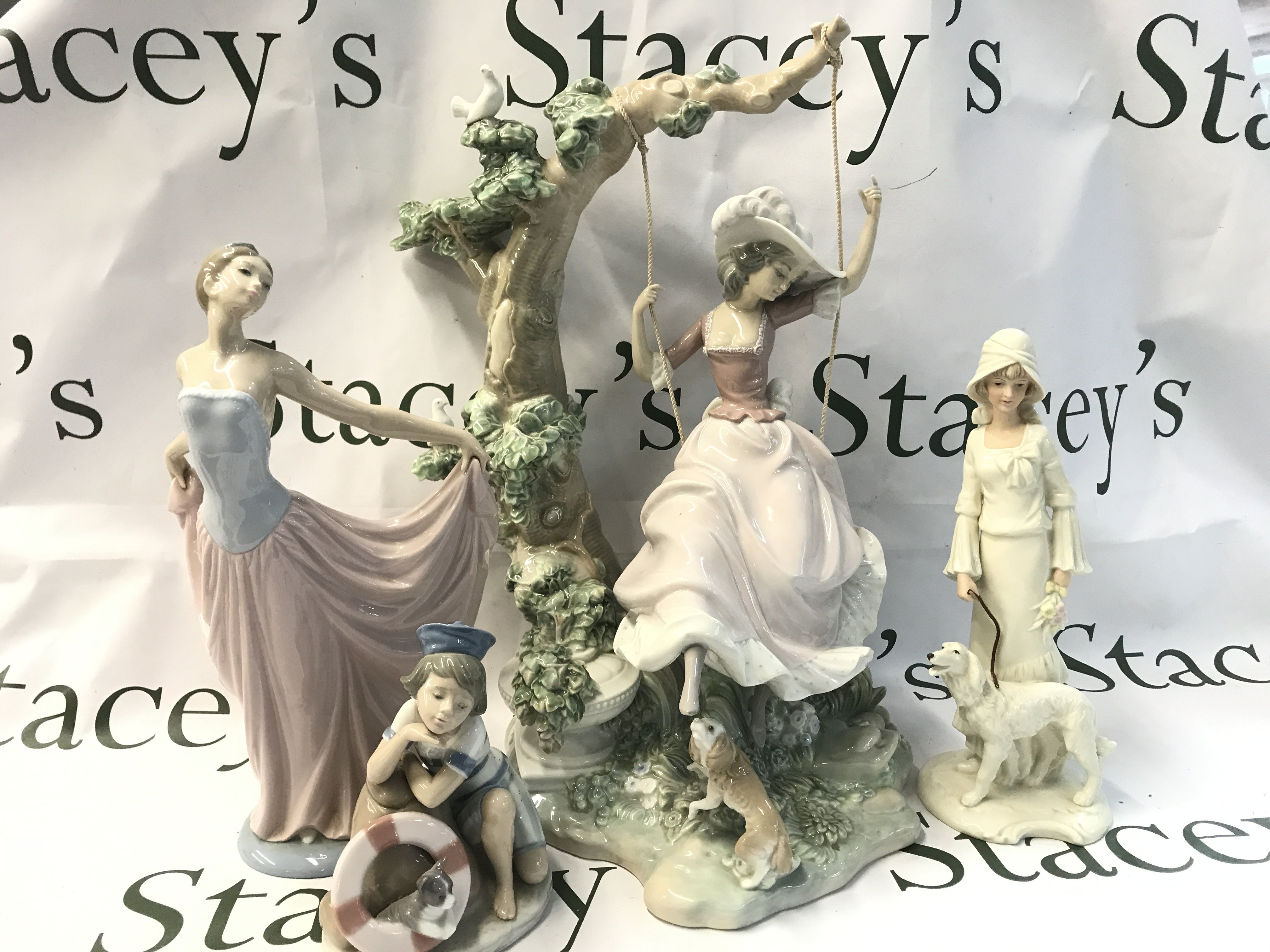 A large Lladro girl on swing figure (40cm tall), Lladro dancer figure, Mondays child sailor boy, SBL pride of place woman with dog figure. This lot cannot be posted