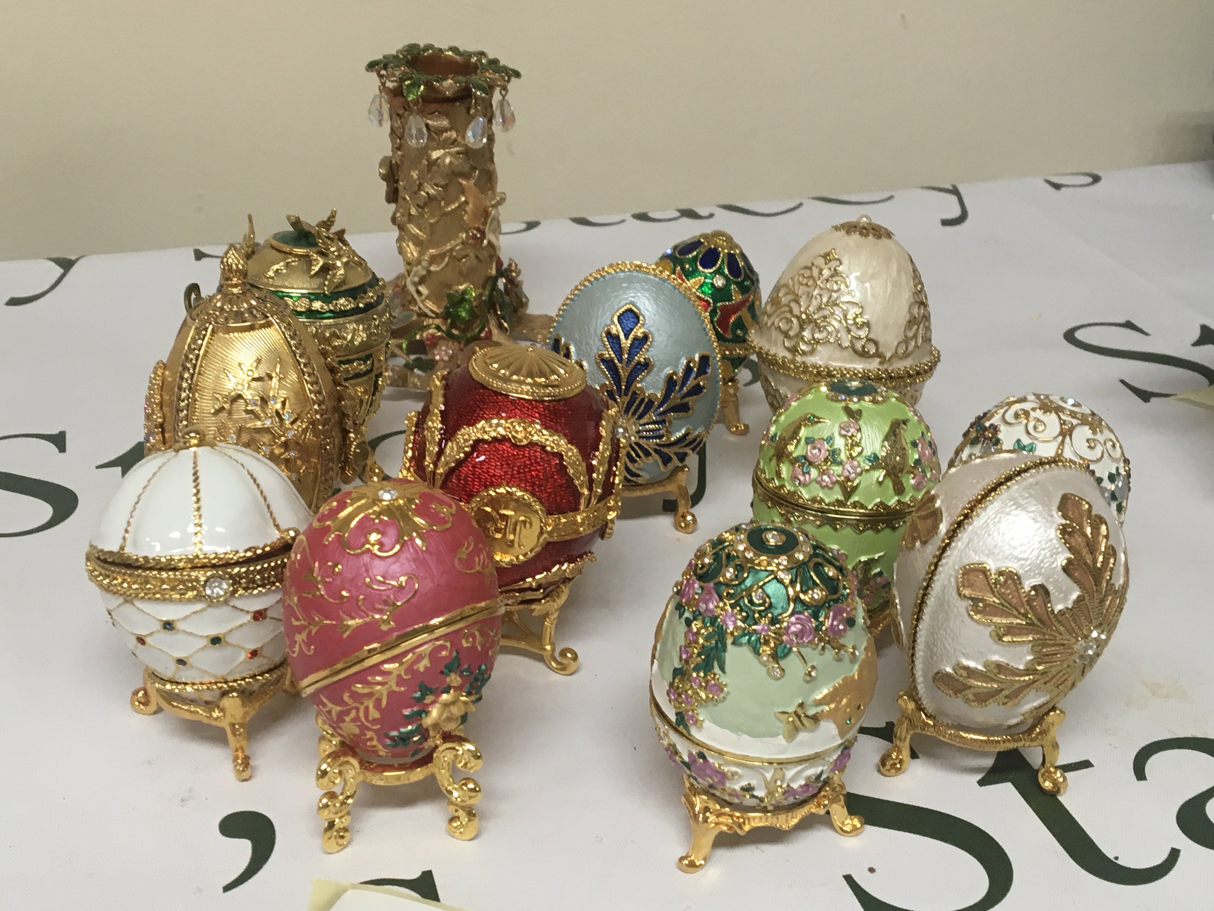 A collection of enamel and gilt metal elaborate egg caskets on small stands set with simulated Jewels and a conforming candle holder.