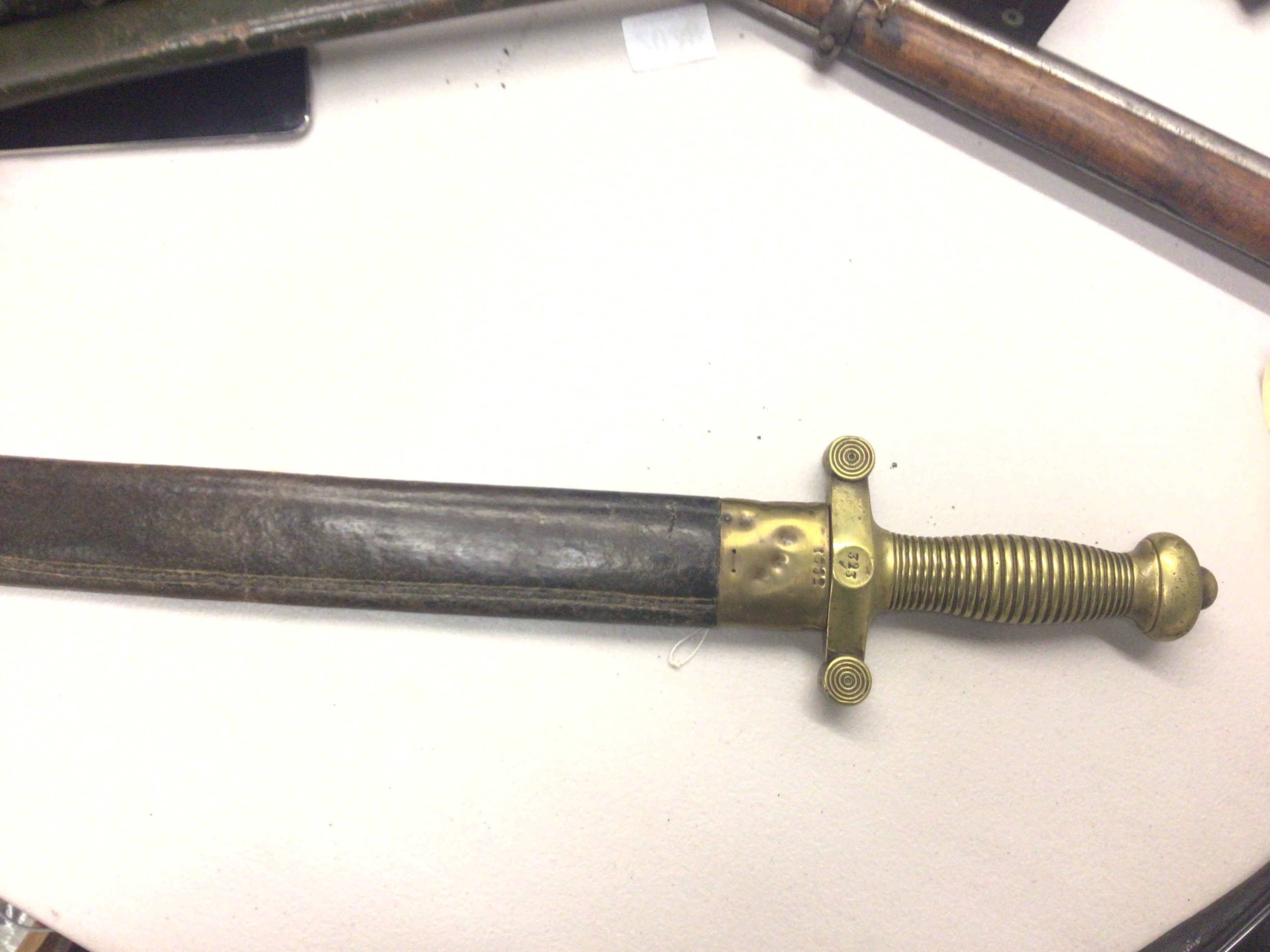 A French 1831 pattern Gladiator type short sword brass grip and steel blade in a leather scabbard with makers marks to the blade also numbered on the hilt 323.