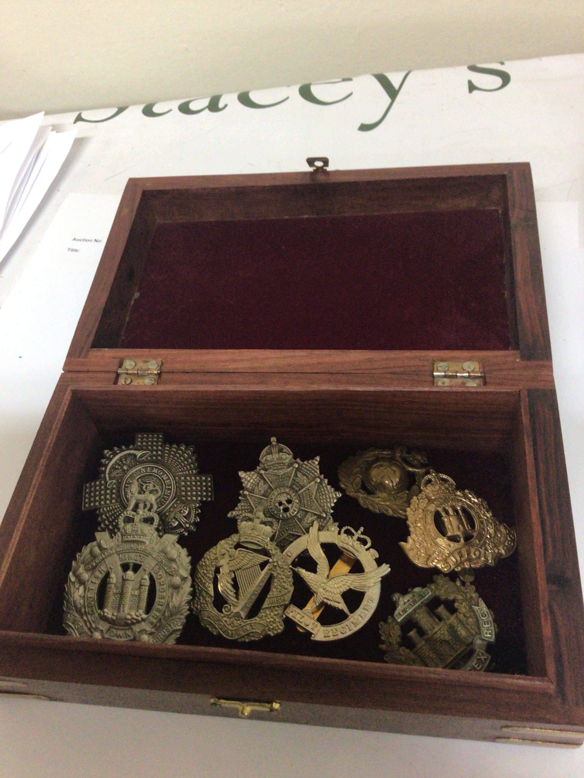 An inlaid hardwood box containing military regimental hat badges.