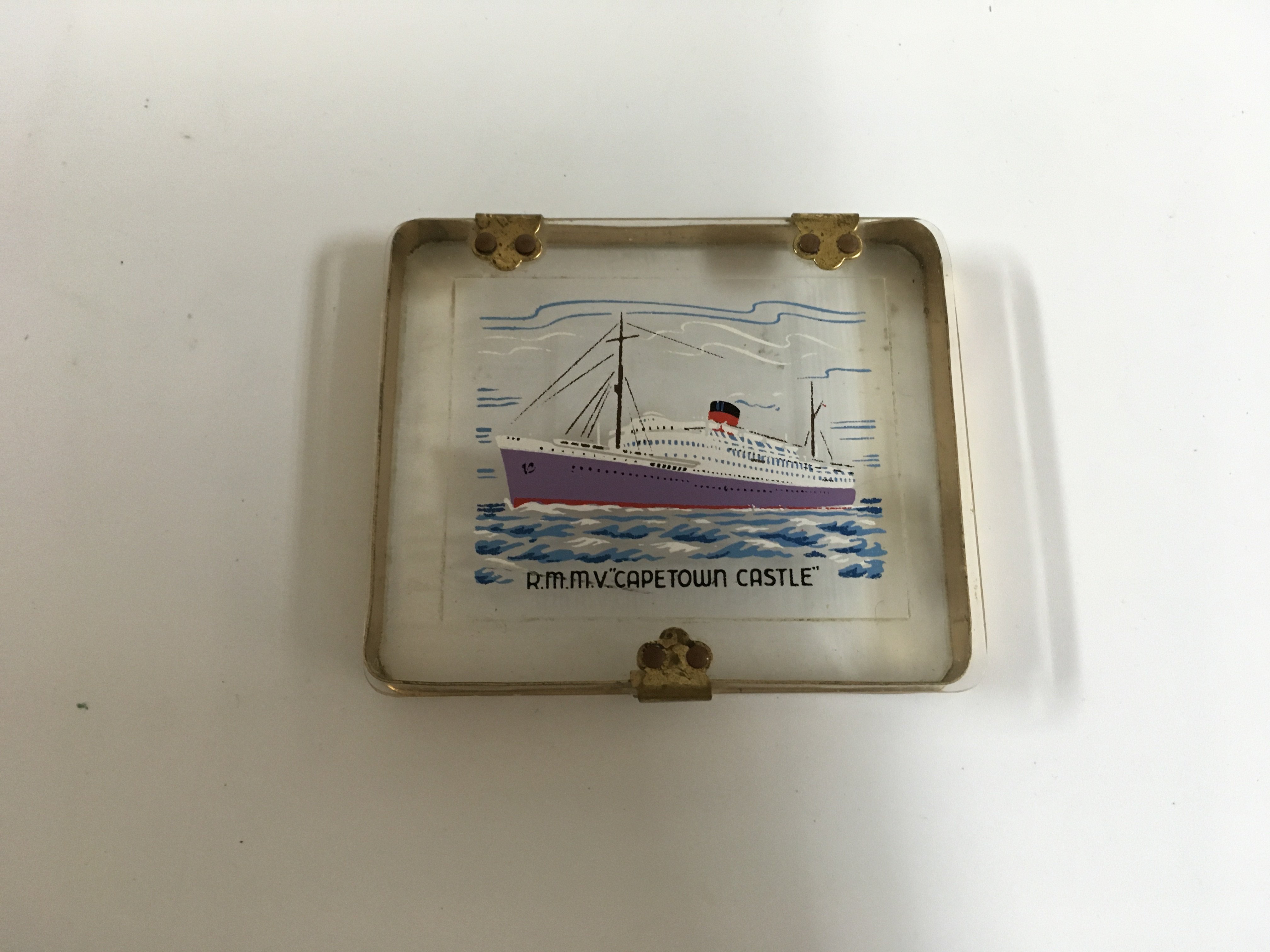 A collection of Union castle line items consisting of a side plate in decorative company pattern from the Union castle line, souvenir chrome ashtray from the Union castle line vessel the RMS Arundel castle, silver plated dining table salt pot from the Union castle line vessel the walmer castle, souvenir cigarette case showing the RMMV Cape Town castle, souvenir tea caddy spoon from the Union castle line vessel the RMMV Athlone castle and very early 1920s design cake stand from the Union castle line