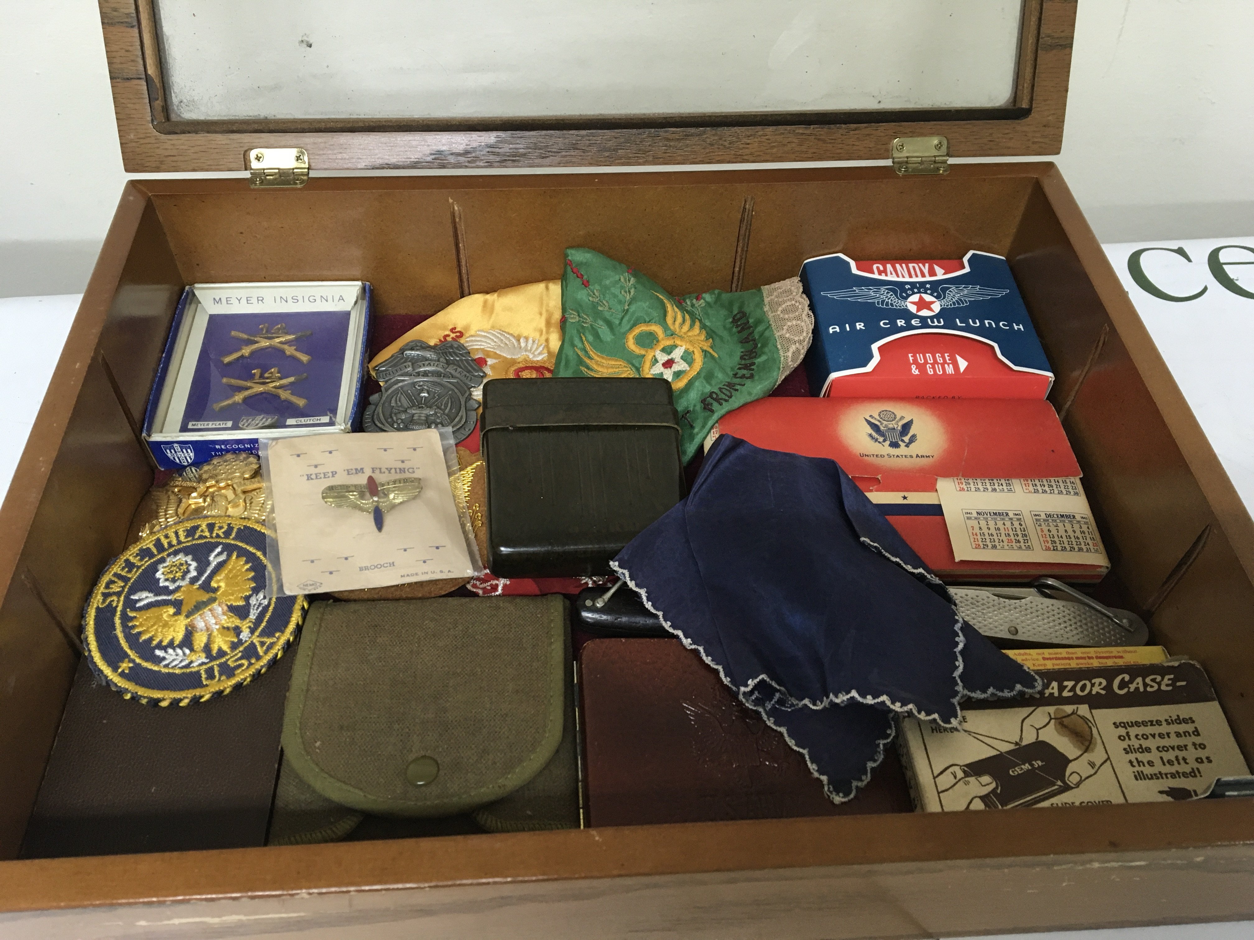 A Case containing American II world war and other items including embroidered silk sweetheart handkerchief badges pocket knifes and other oddments.