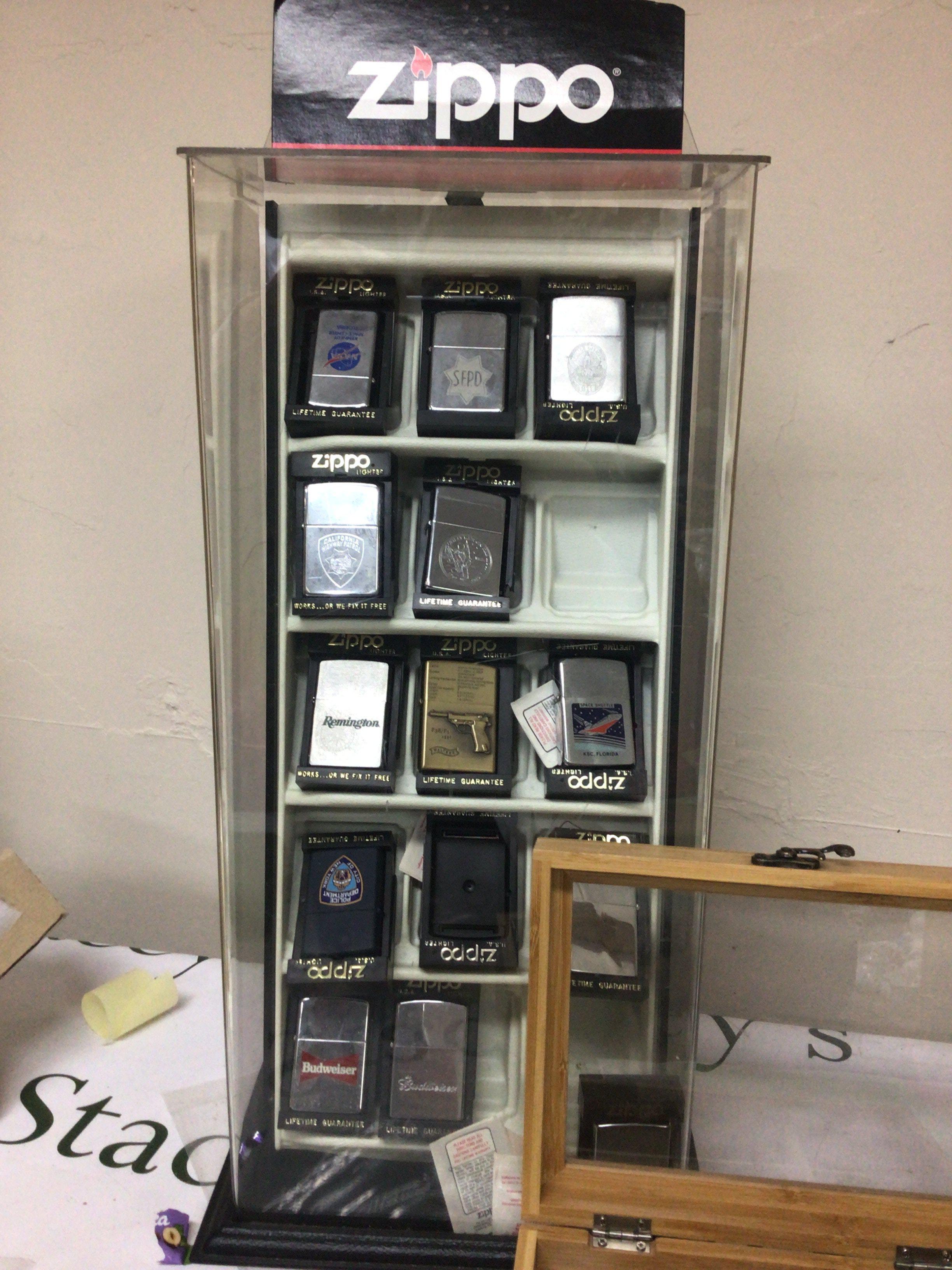 A display case containing Zippo lighters American Police theme and others and collection of conforming lighters in a box.