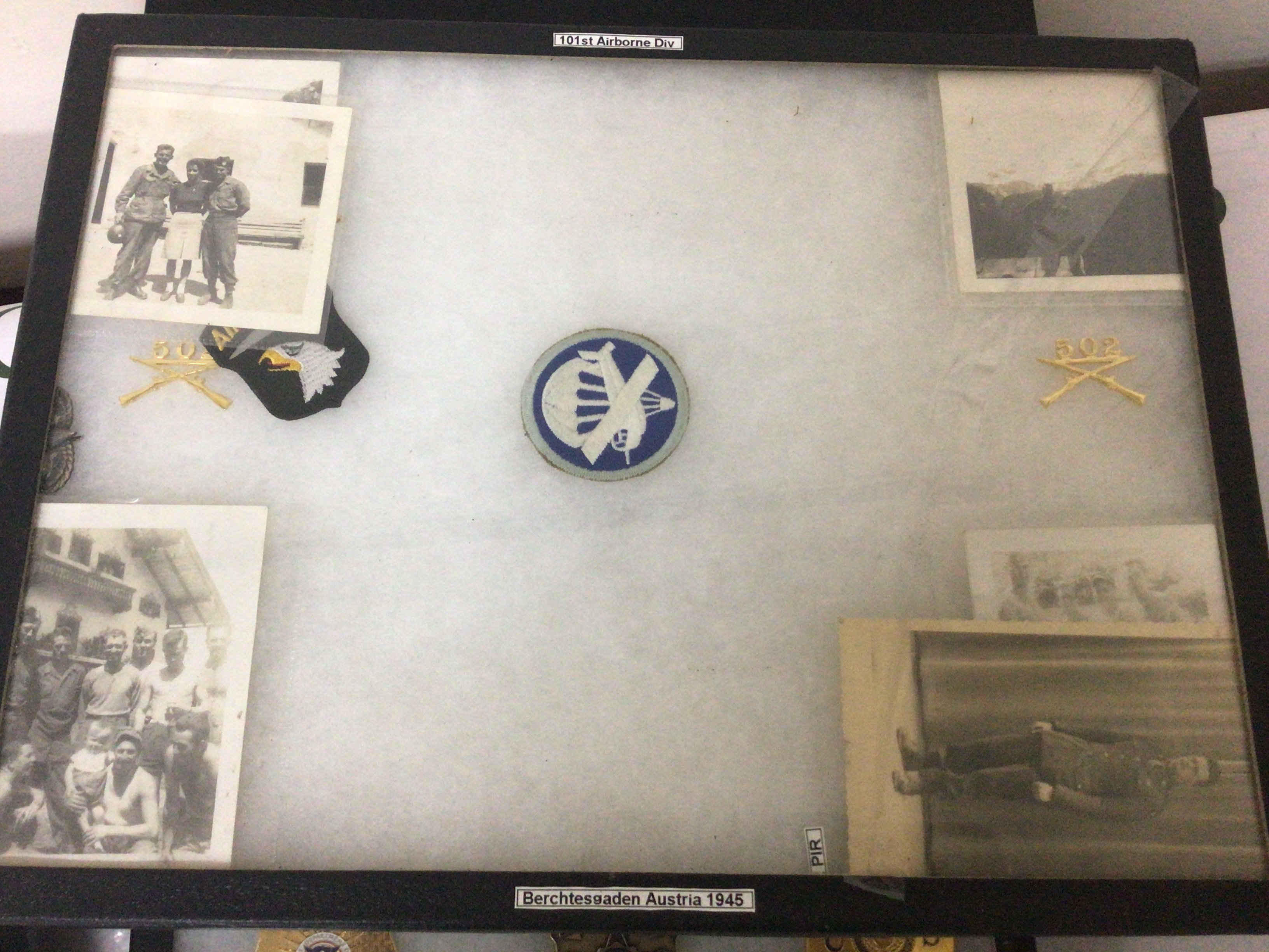 A framed display containing American II world war photos including some of personal from 101 Airborne division. A letter to the troops Allied Expeditionary Force American police badges and other cloth badges.