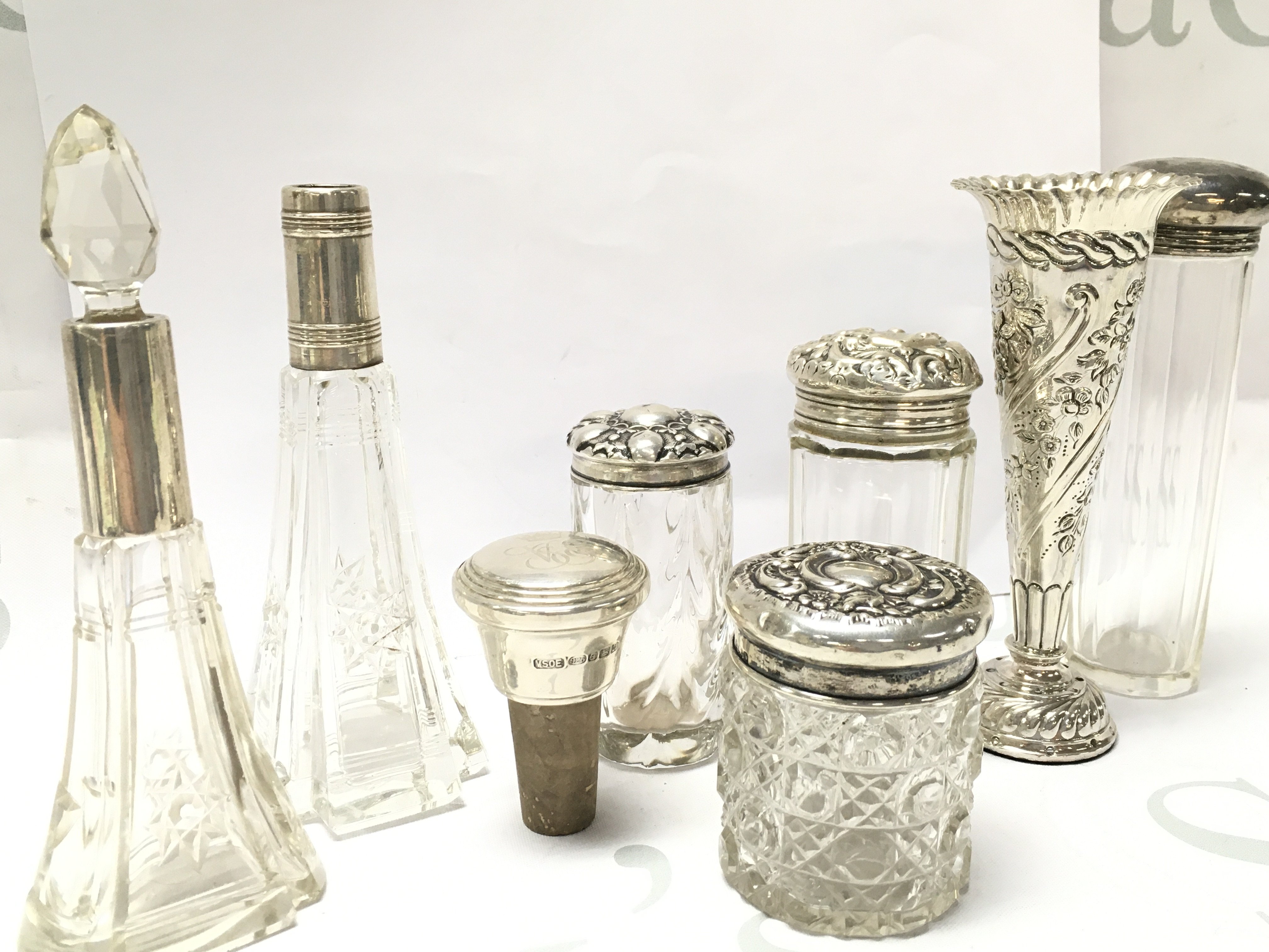 A collection of cut glass Perfume bottles with silver lids and collars , a silver vase , cork silver bottle stopper. This lot cannot be posted