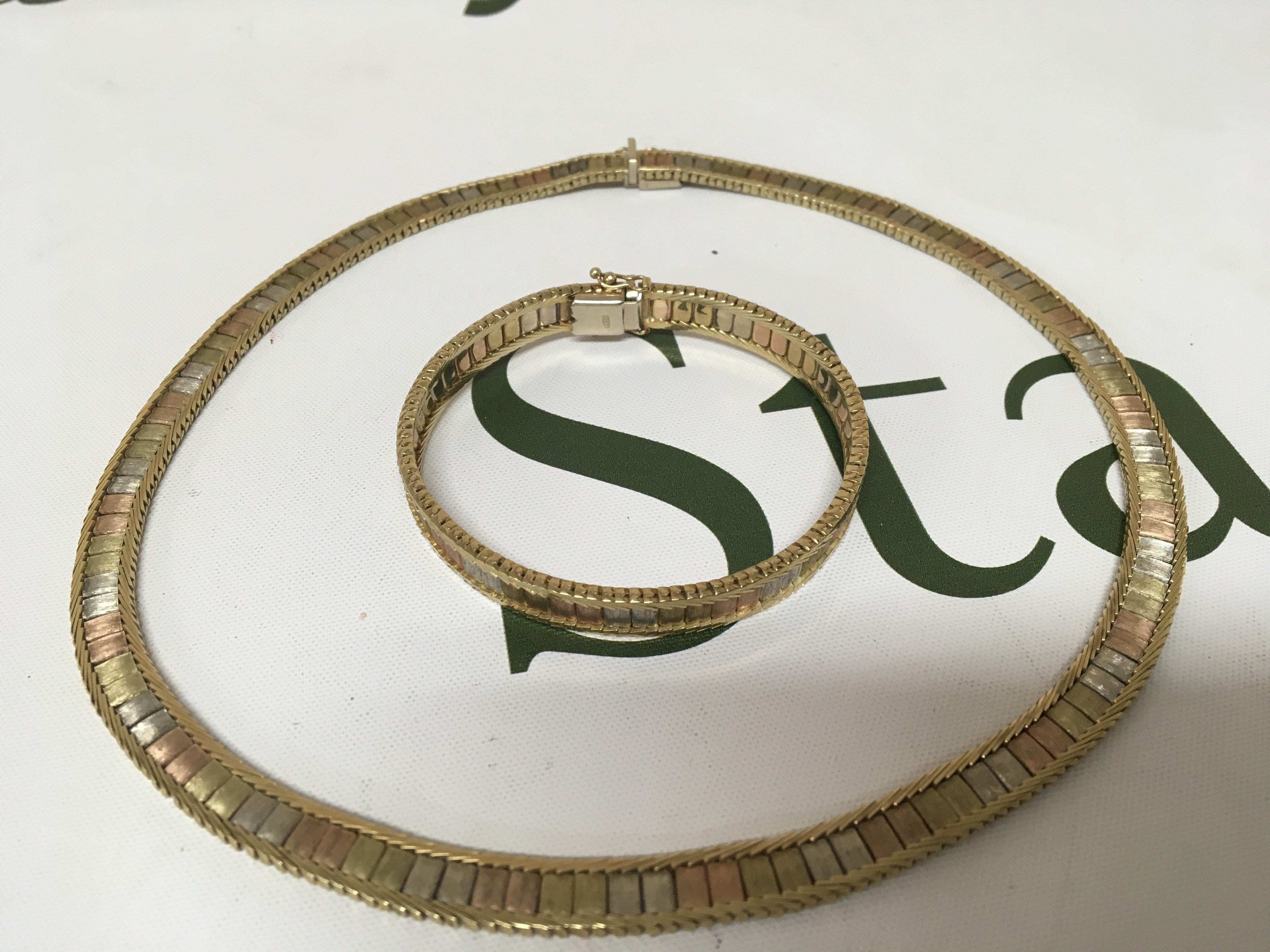 A gold necklace and matching bracelet the centre enclosed links with alternating three tone colour links both bracelet and necklace marked 9carat. Total weight 57g approximately.