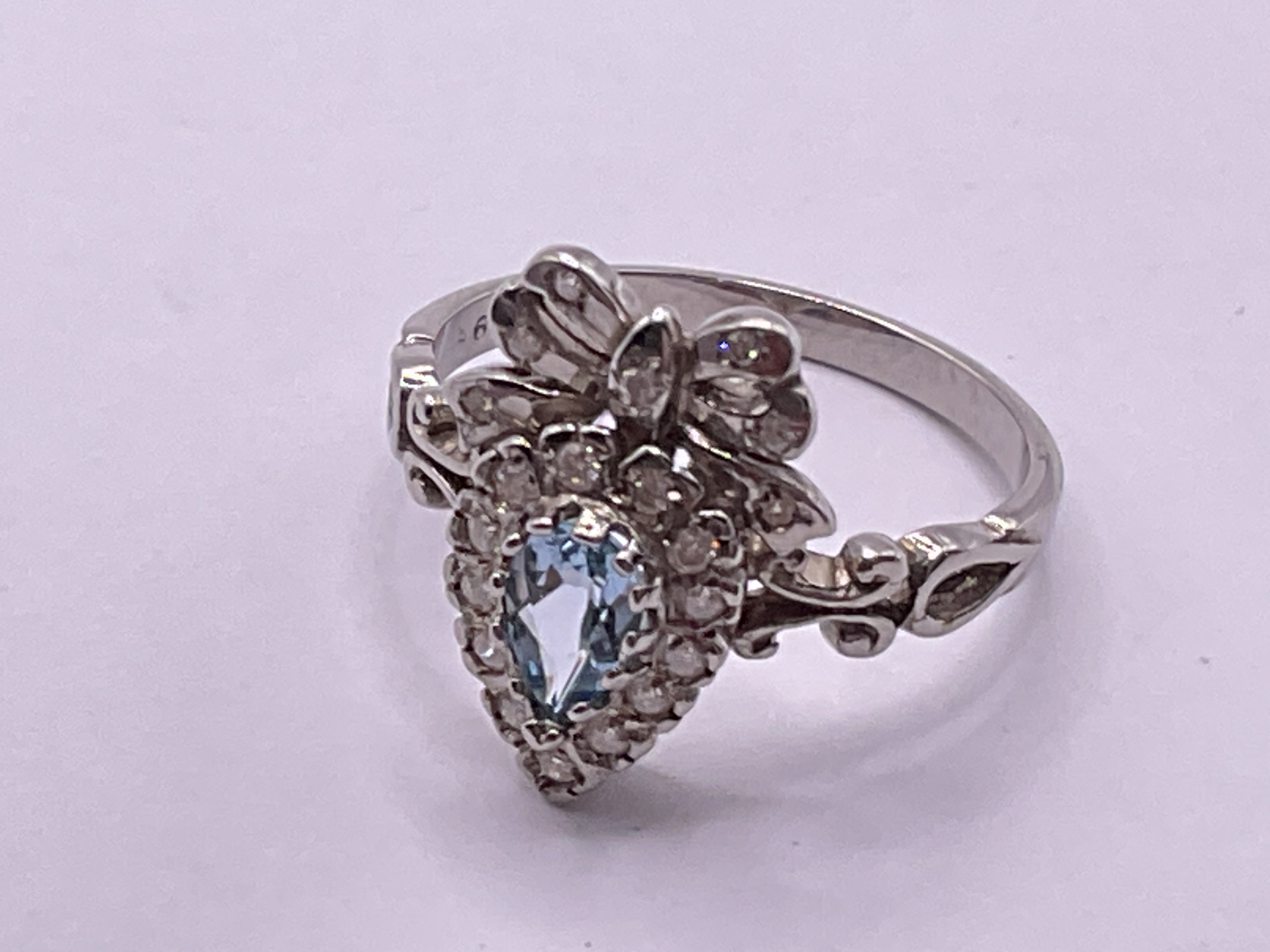 9ct white gold bow style ring set with pear shaped blue topaz and RBC diamonds. Topaz 0.30ct. Diamonds 0.20ct. Ring size approx N. Postage category A.