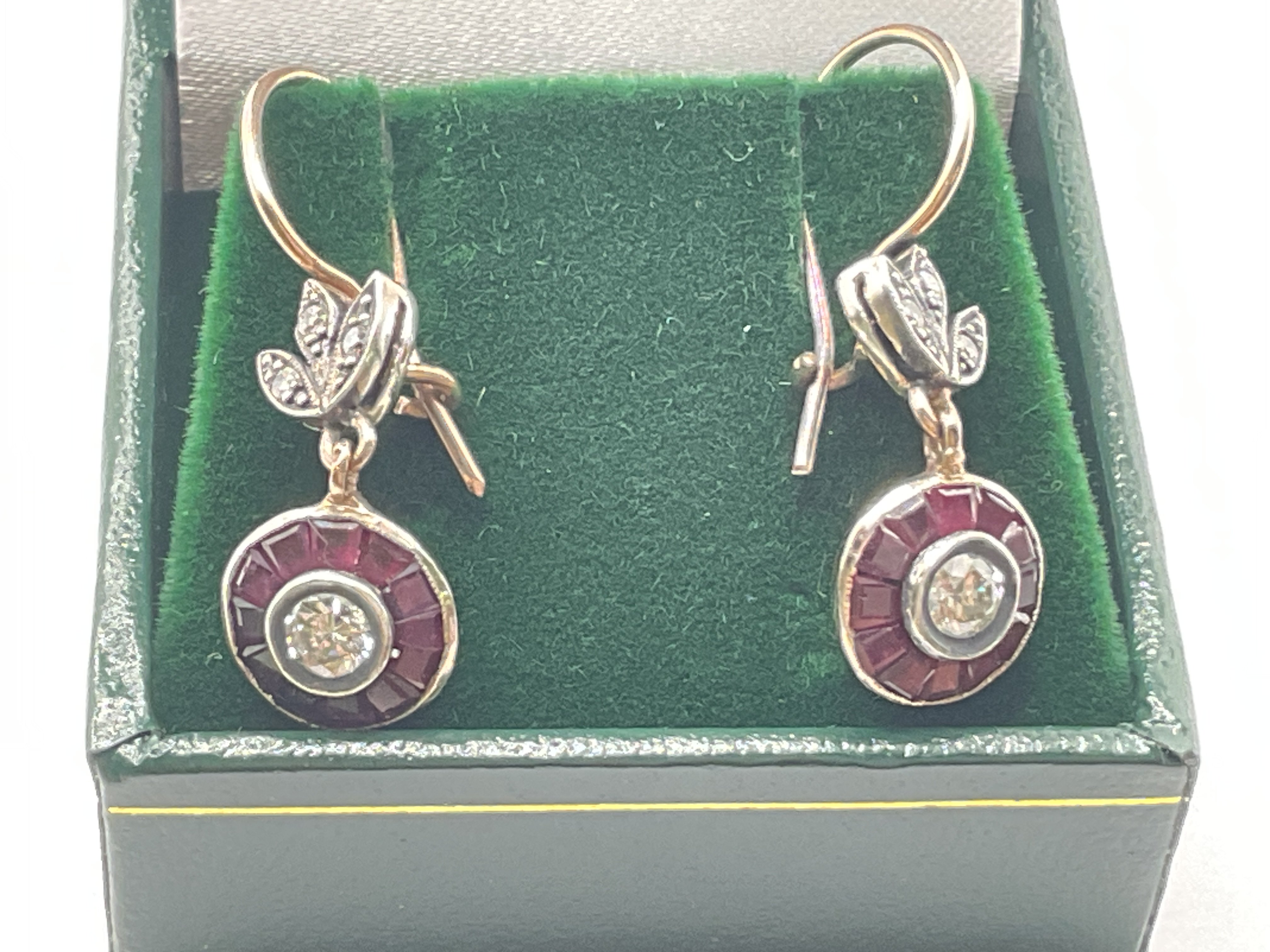 Pair of 8ct rose gold fish hook target style drop earrings set with R/C diamonds surrounded by calibre cut rubies, with further diamonds in the bales, boxed. Rubies 0.58ct approx. Diamonds 0.60ct approx. Postage category A.