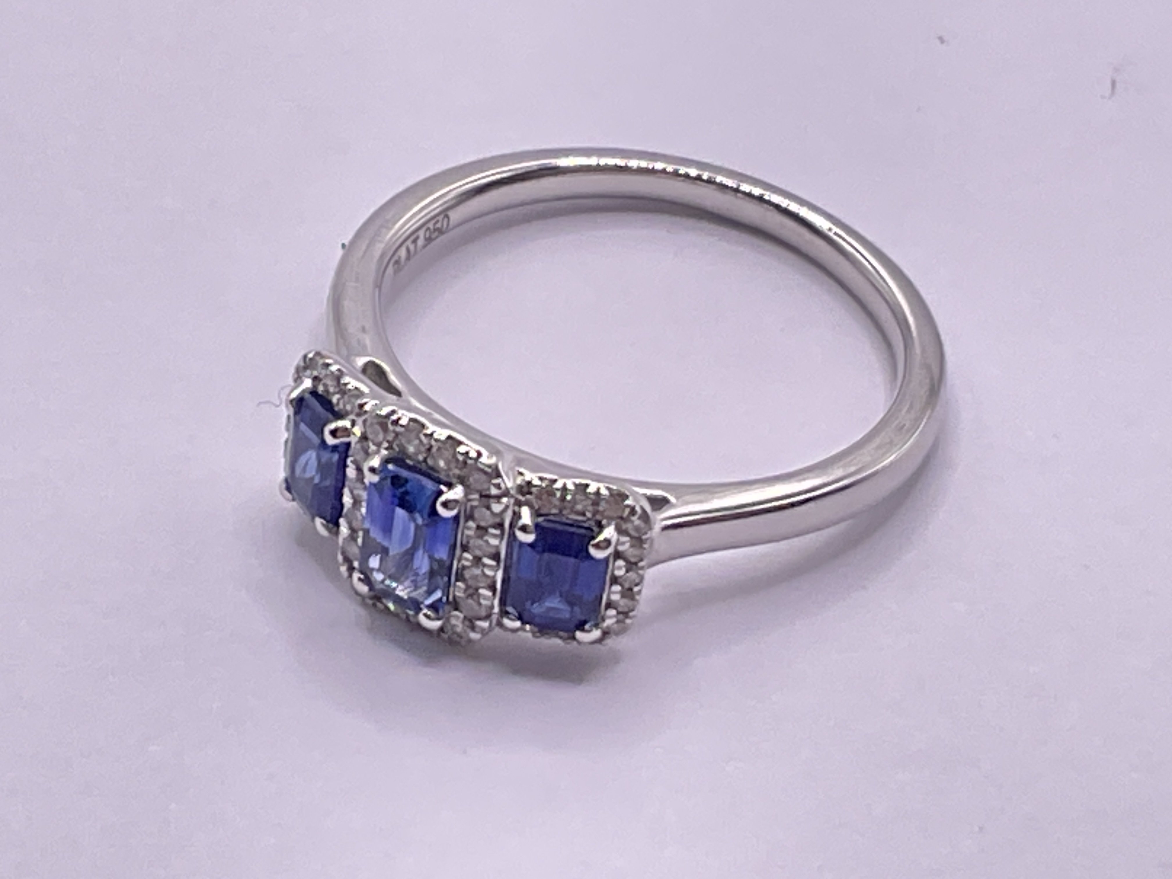 Platinum trilogy ring set with step cut sapphires each surrounded by RBC diamonds. Sapphires 0.83ct. Diamonds 0.14ct. Ring size approx M. Postage category A.