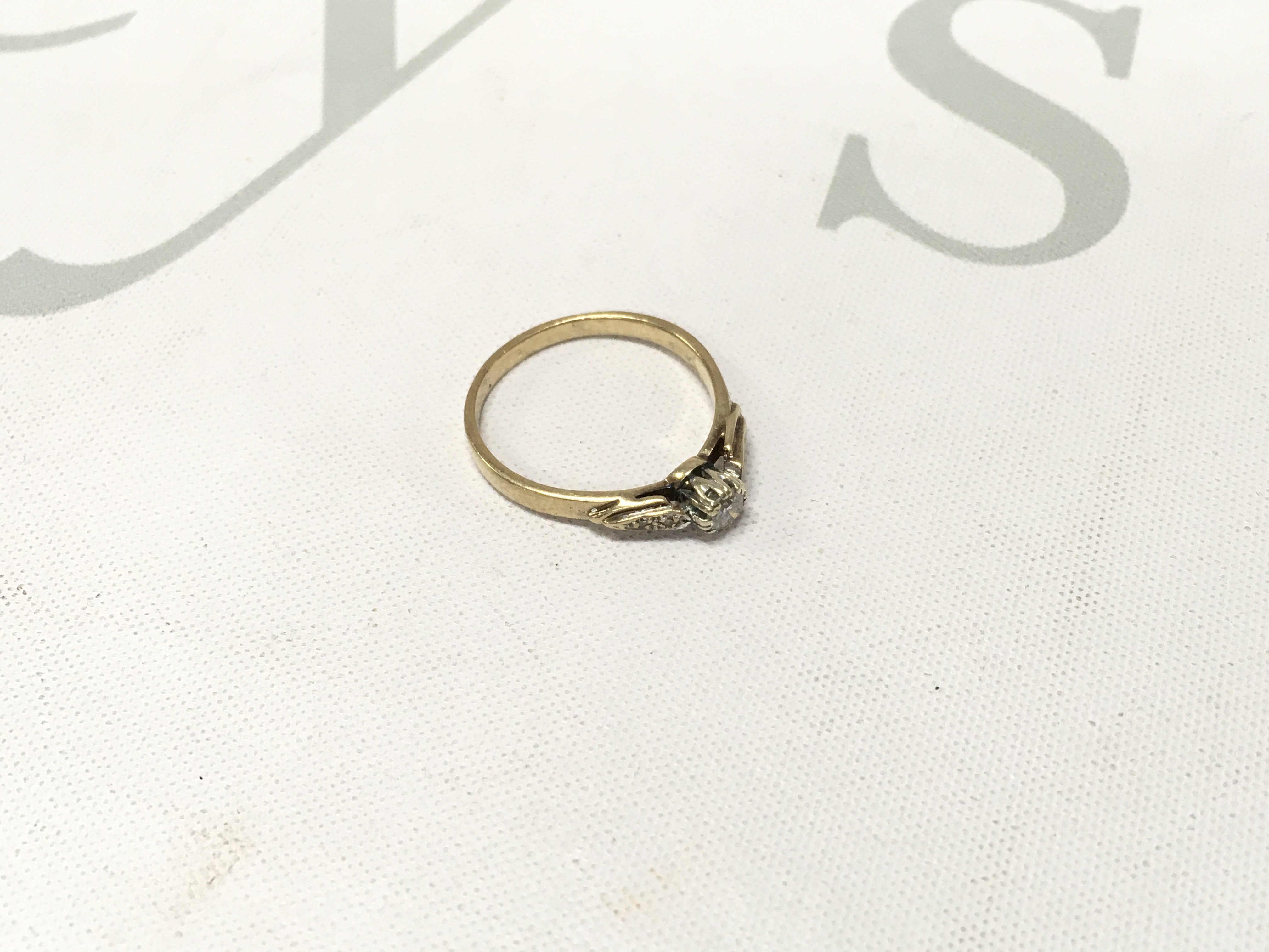 A gold solitaire ring with stone set shoulders.