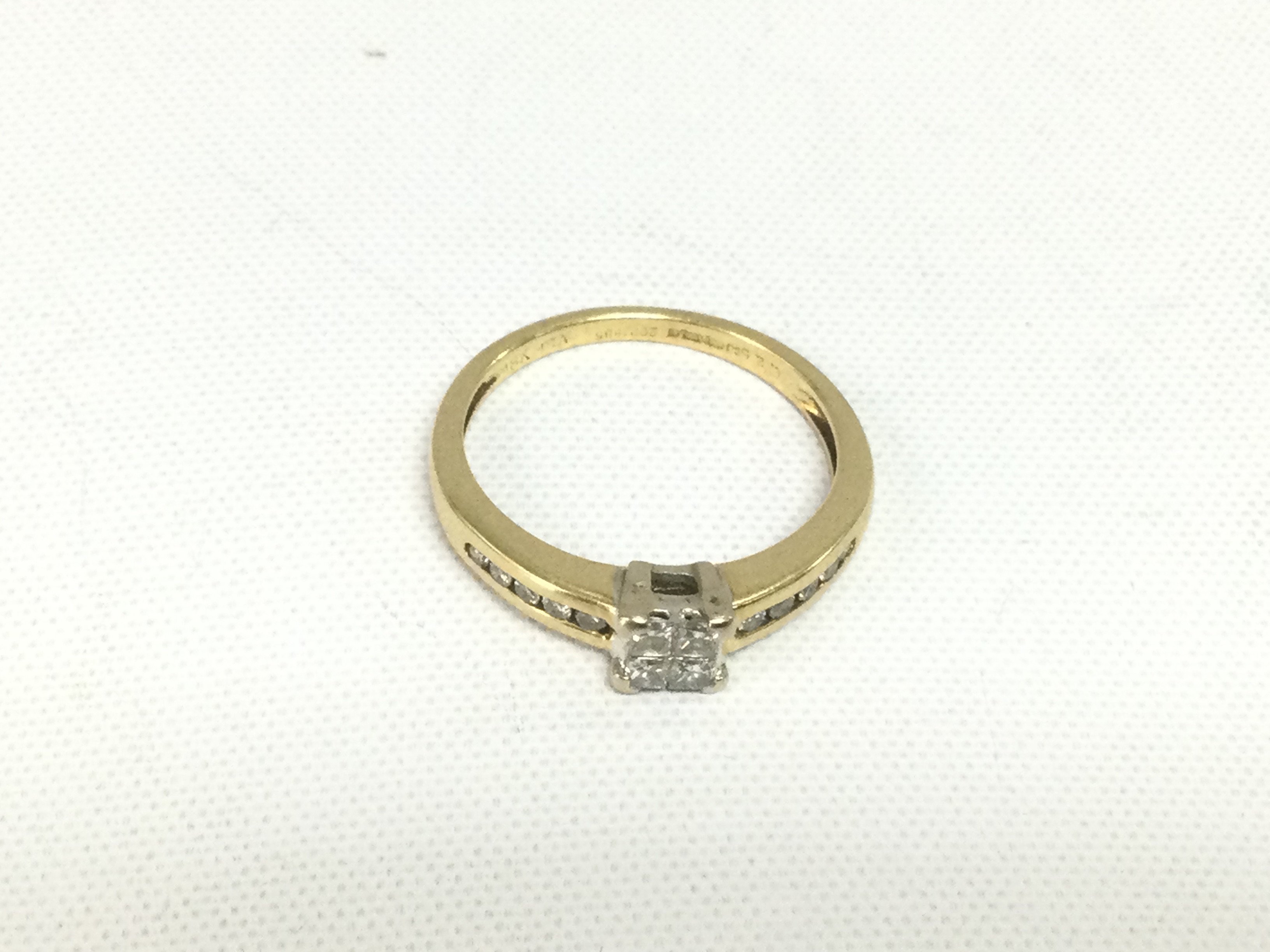 An 18ct gold diamond ring set with four central princess cut diamonds and smaller diamonds to the shoulders, approx 2.8g and approx size L-N. Shipping category A.