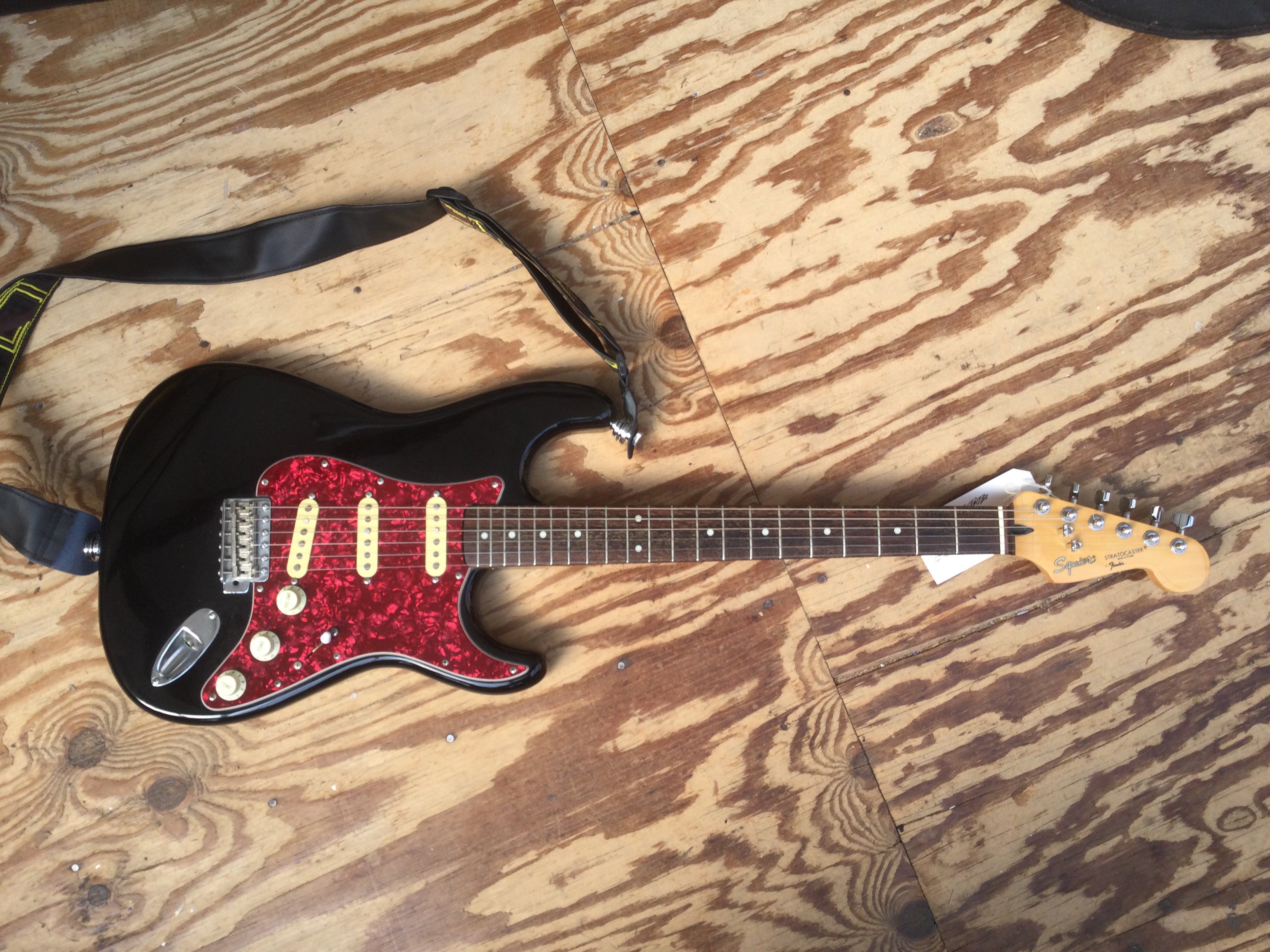 A Fender Squier Stratocaster in black with a red tortoiseshell pickguard. No case.