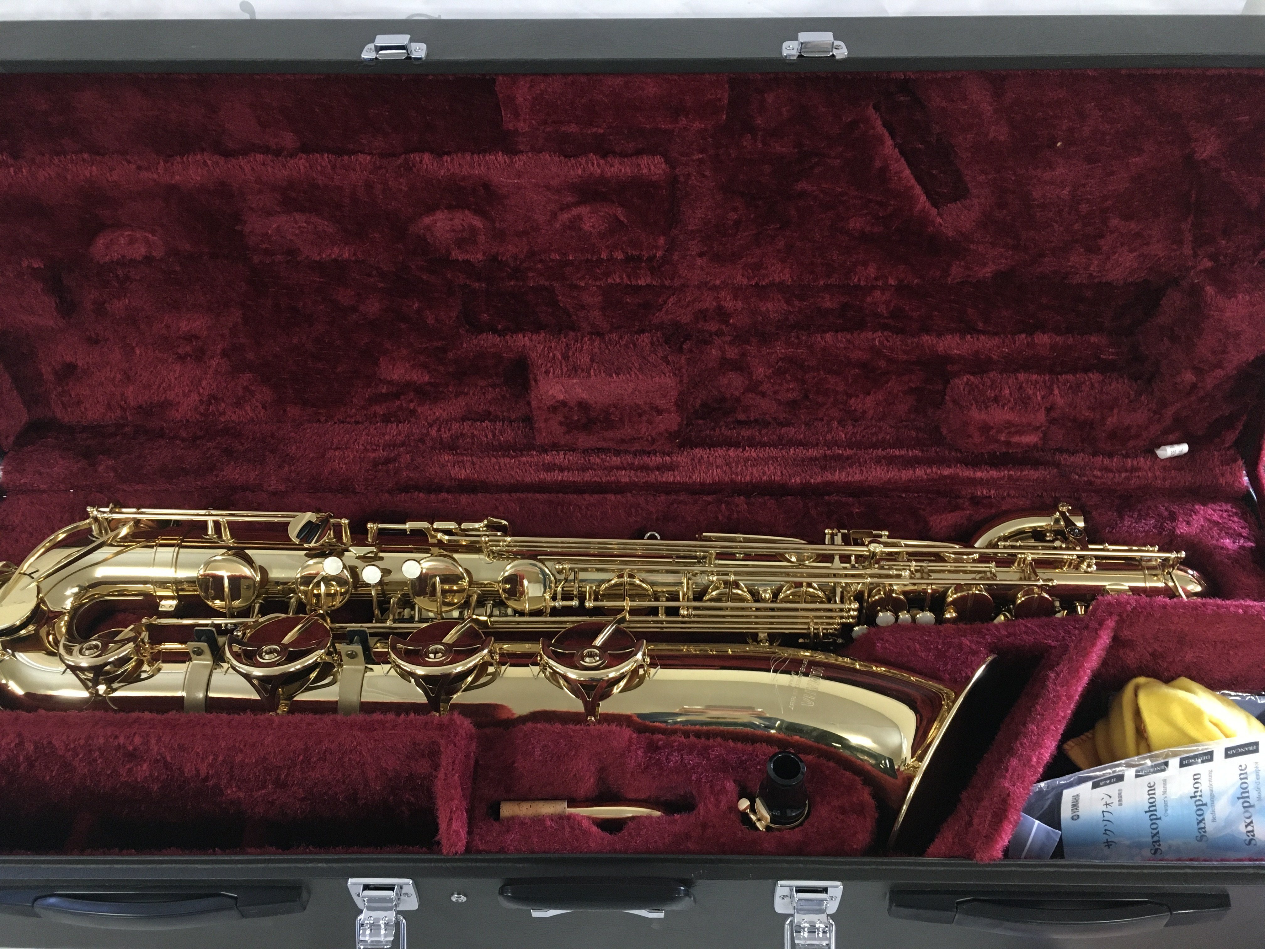 A cased Yamaha baritone saxophone with accessories and stand.