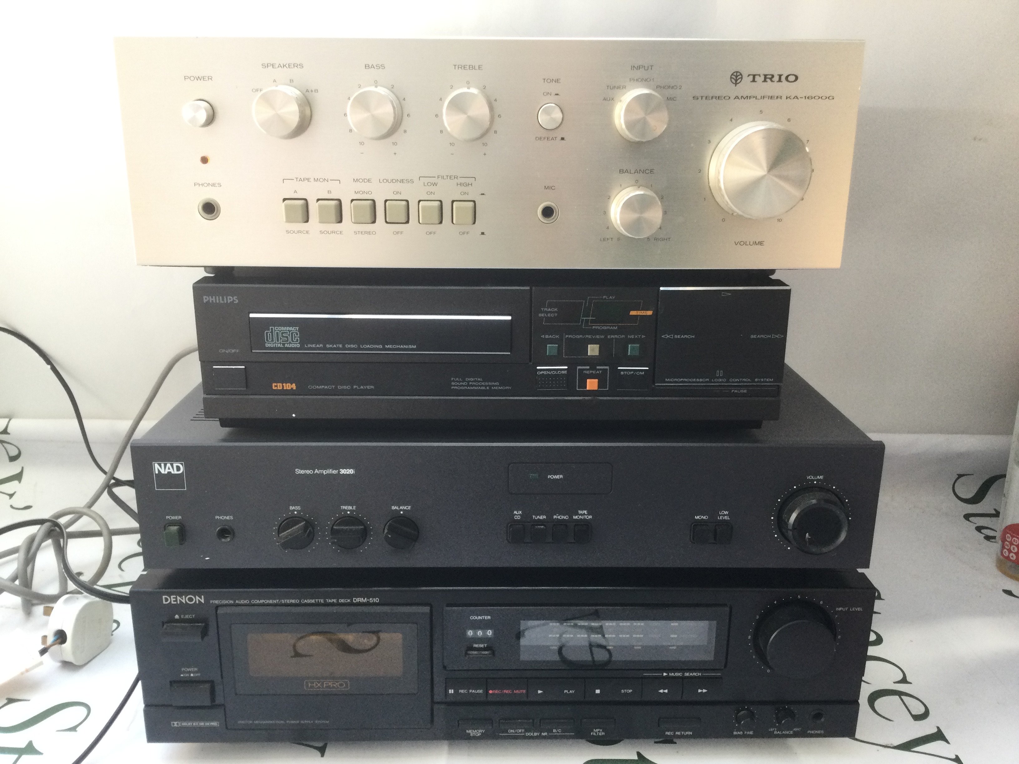 A Trio KA-1600G amplifier, a boxed NAD 3020i amp, boxed Philips CD104 CD player and a boxed Denon DRM-510 cassette deck. Includes some manuals.