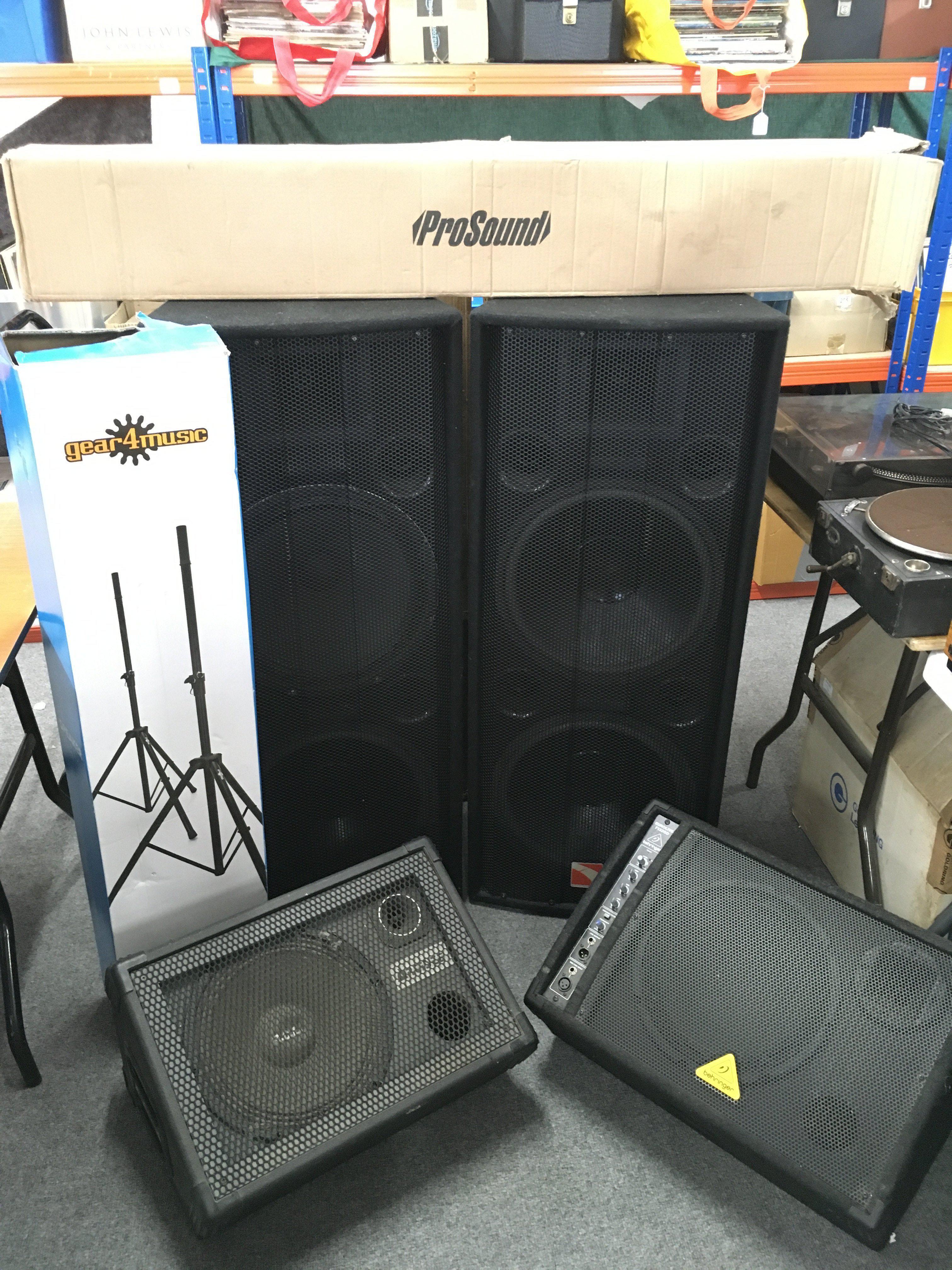 A collection of PA system equipment comprising a boxed Behringer Eurorack MX3242X 32 input mixing console, a pair of boxed Intimidation AKA 215 MKII speakers, two wedge monitors and stands.