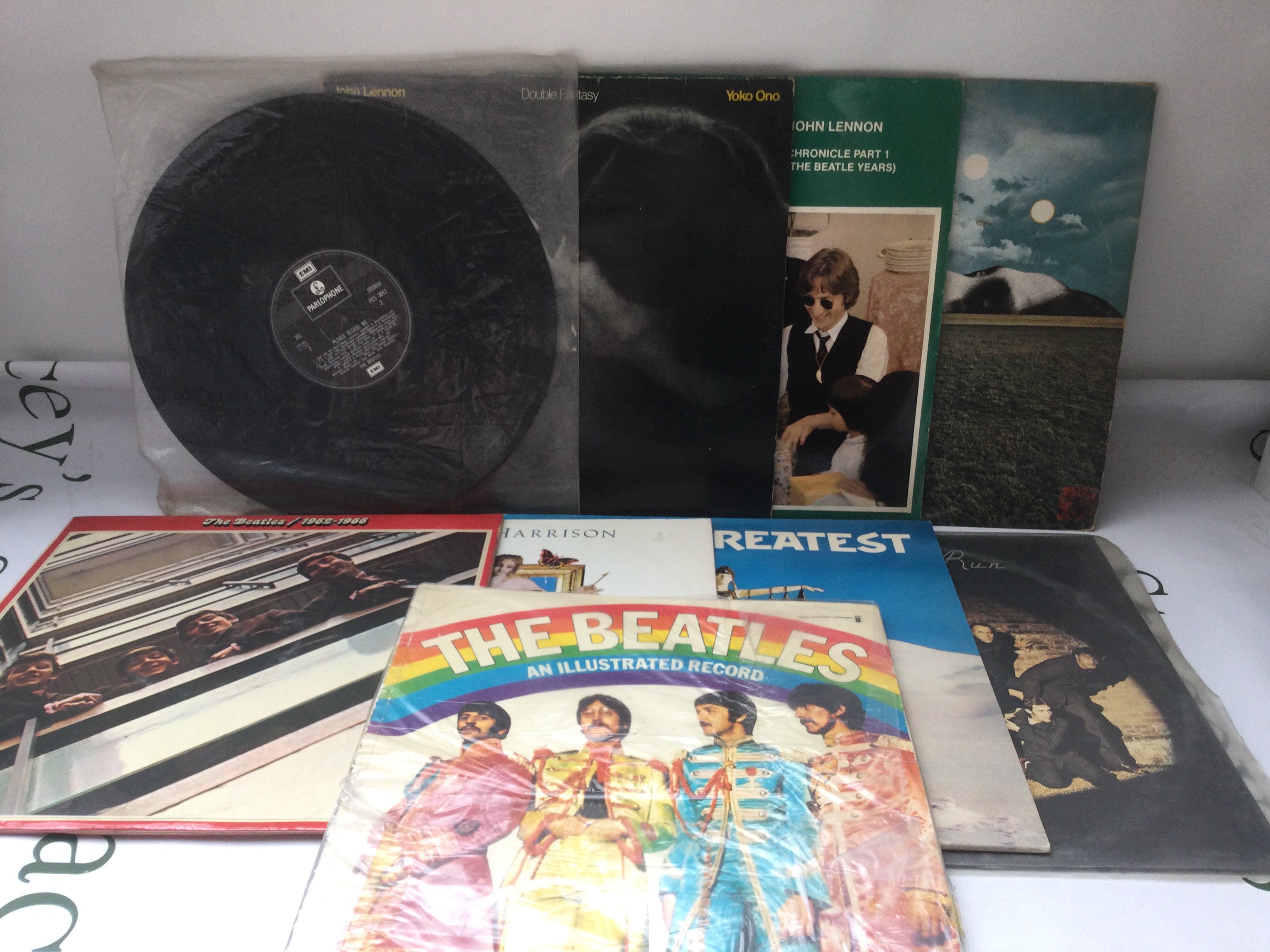 Two bags containing sixteen Beatles and related LPs and 12" singles including a side loading numbered White Album (no portraits), a US Capitol issued Magical Mystery Tour, Mind Games and others. Plus a Beatles book.