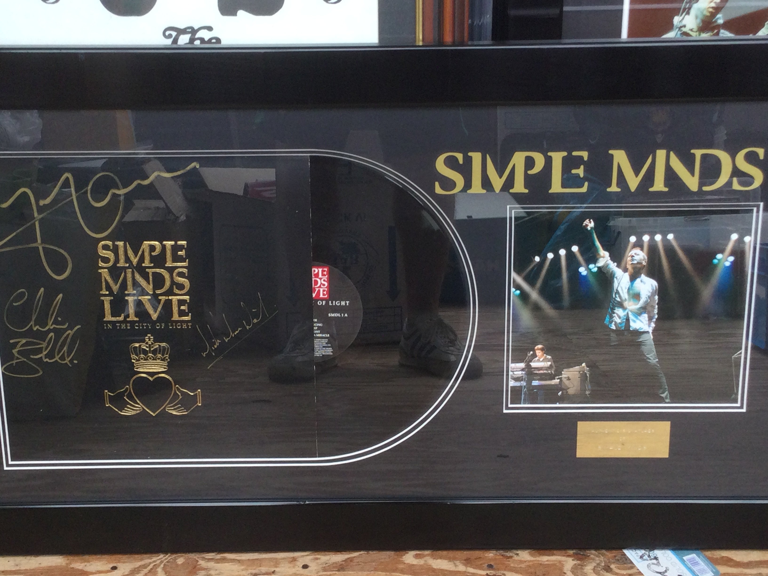 A framed and glazed Simple Minds display signed by Jim Kerr, Charlie Burchill and Mick MacNeil, approx 50.5cm x 91cm.