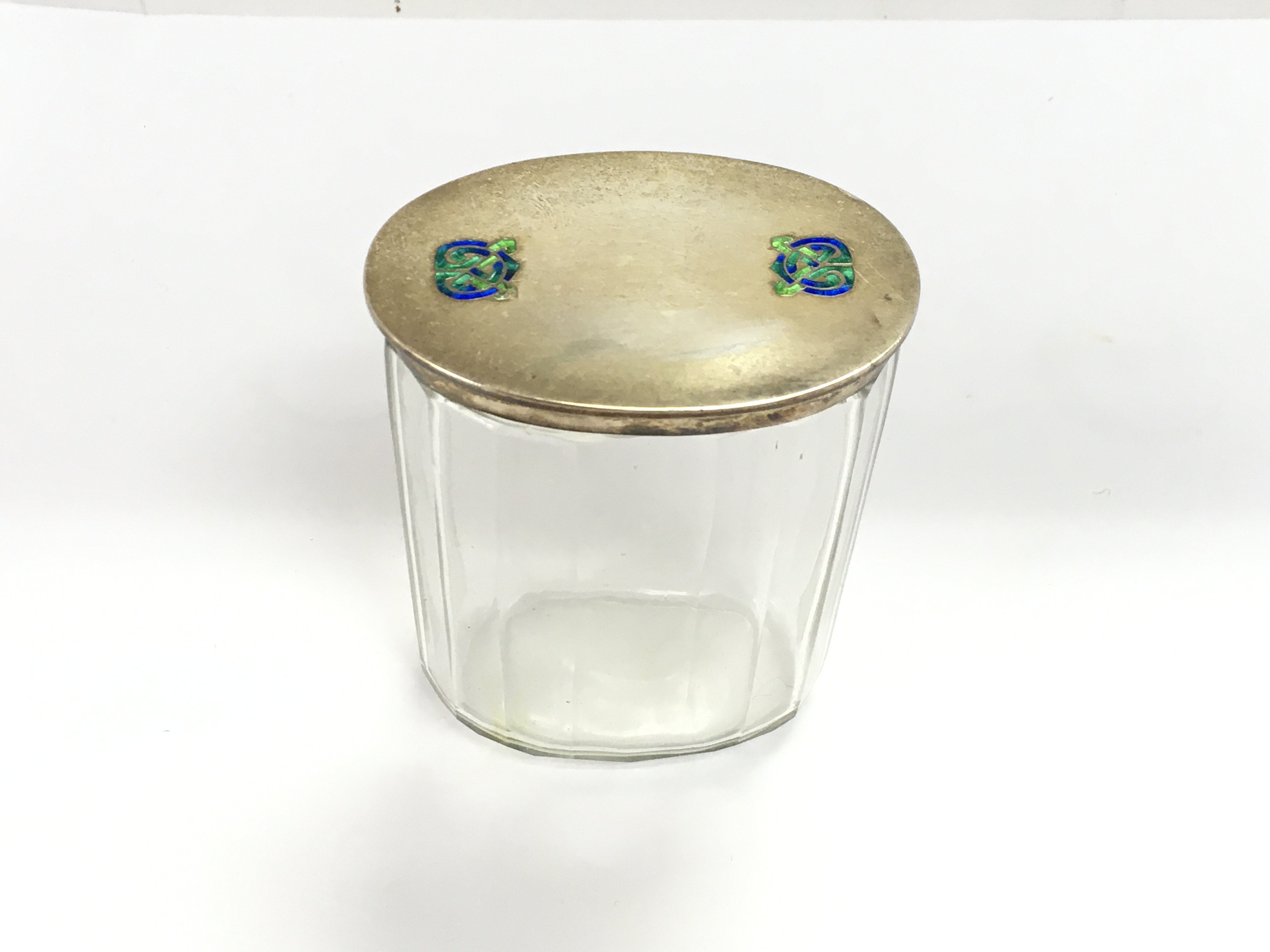 A Liberty and co Archibald knox silver lidded glass dressing table jar with celtic enamel circa 1915. Good condition but very small amount of enamel missing.