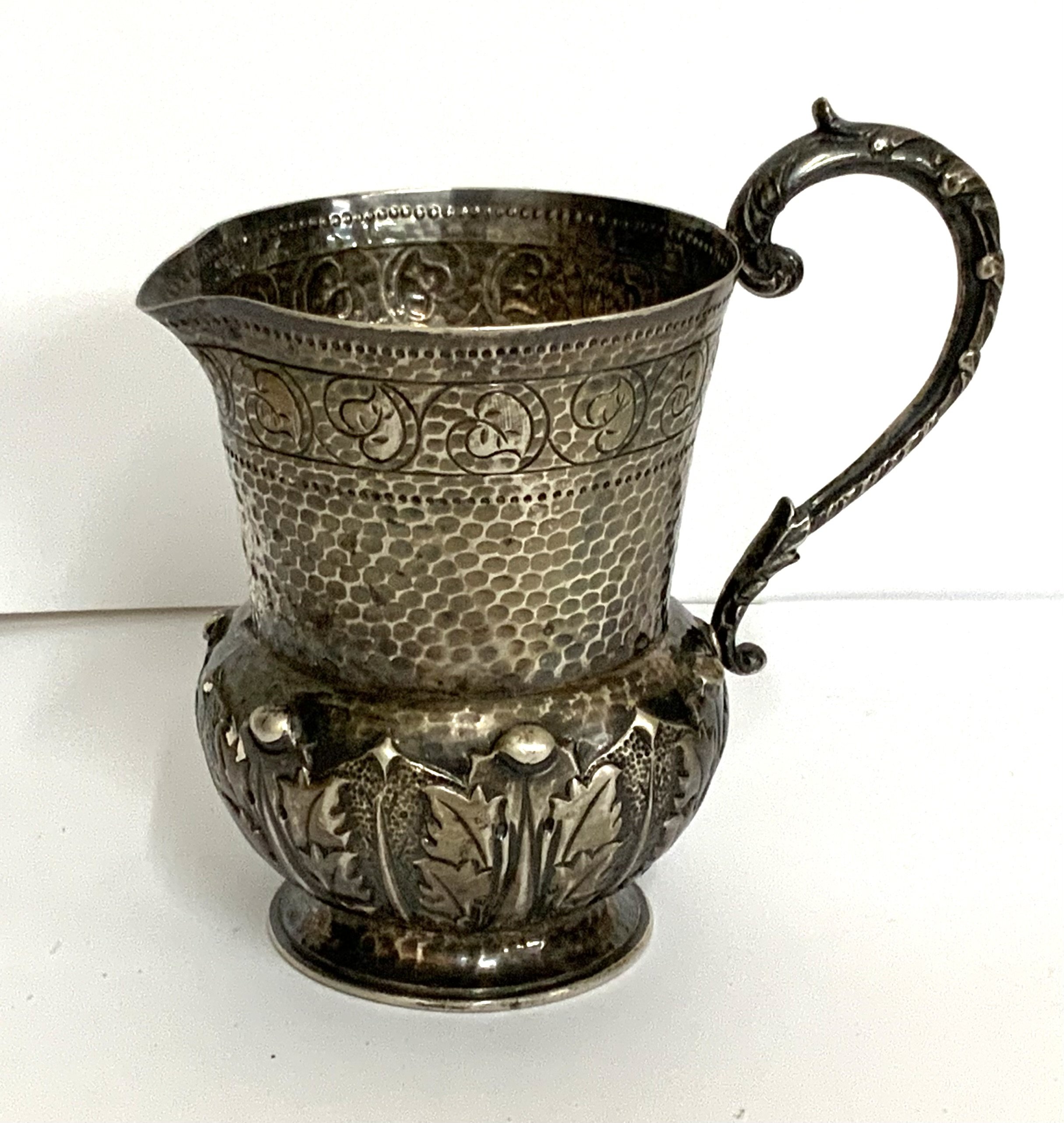 A small hallmarked silver jug with acanthus leaf decoration and hammered decoration. marks for London, 1900 Goldsmith alliance marks S.S (12cm) (A).