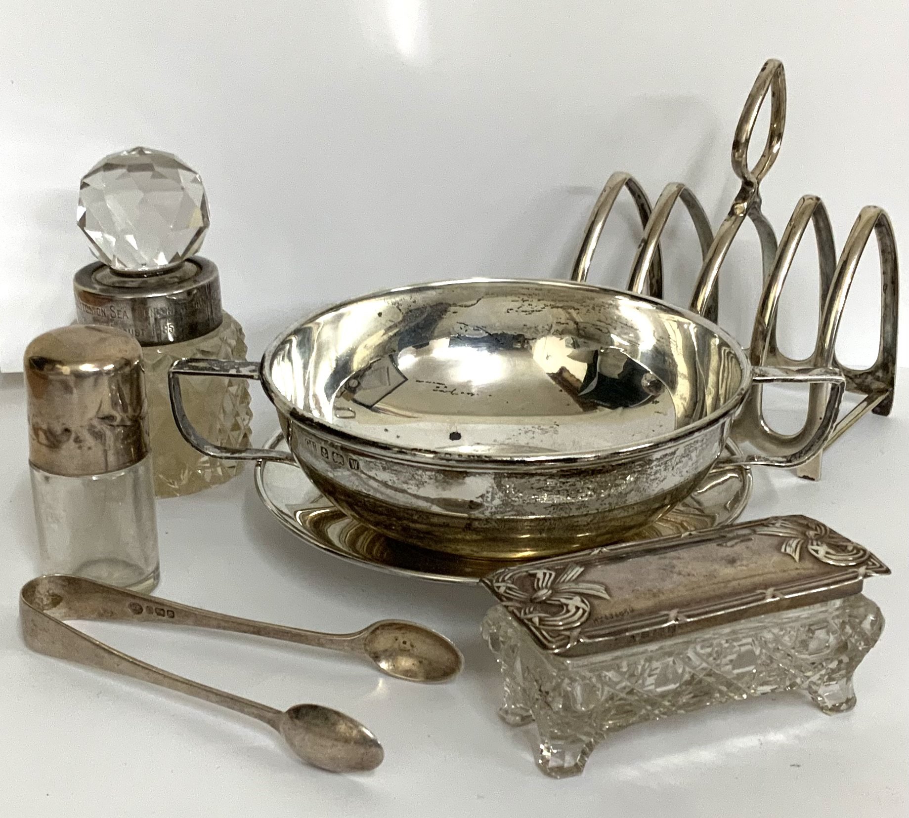 A two handled silver soup bowl and saucer, marks for Birmingham 1921, George Unite. Together with hallmarked silver toast rack, trinket box, smelling slats bottle, perfume bottle, sugar tongs. (B)
