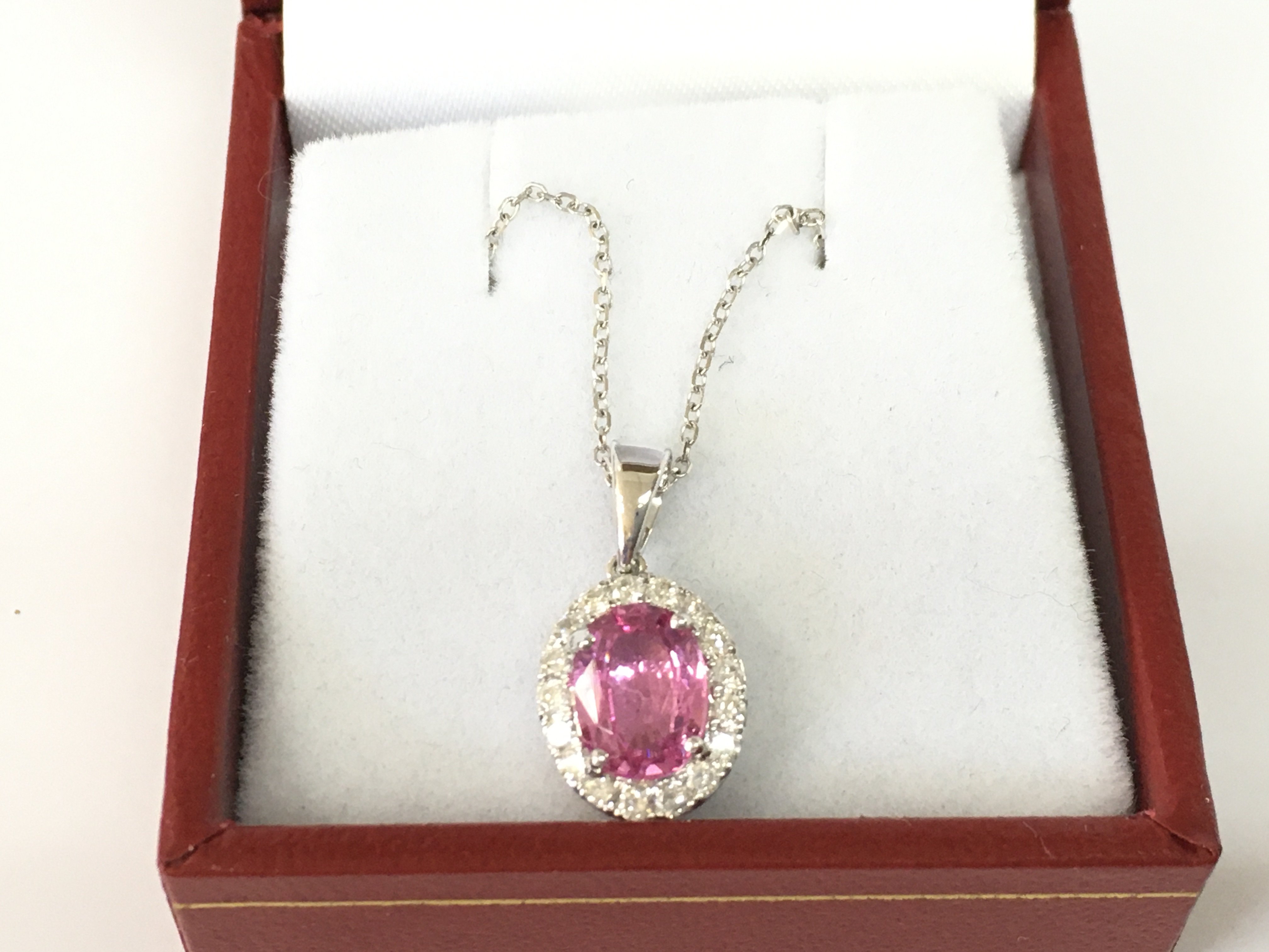 An 18ct white gold oval pink sapphire and RBC diamond cluster pendant on an 18ct whote gold chain. Pink sapphire 1.47ct and 0.27ct diamonds.