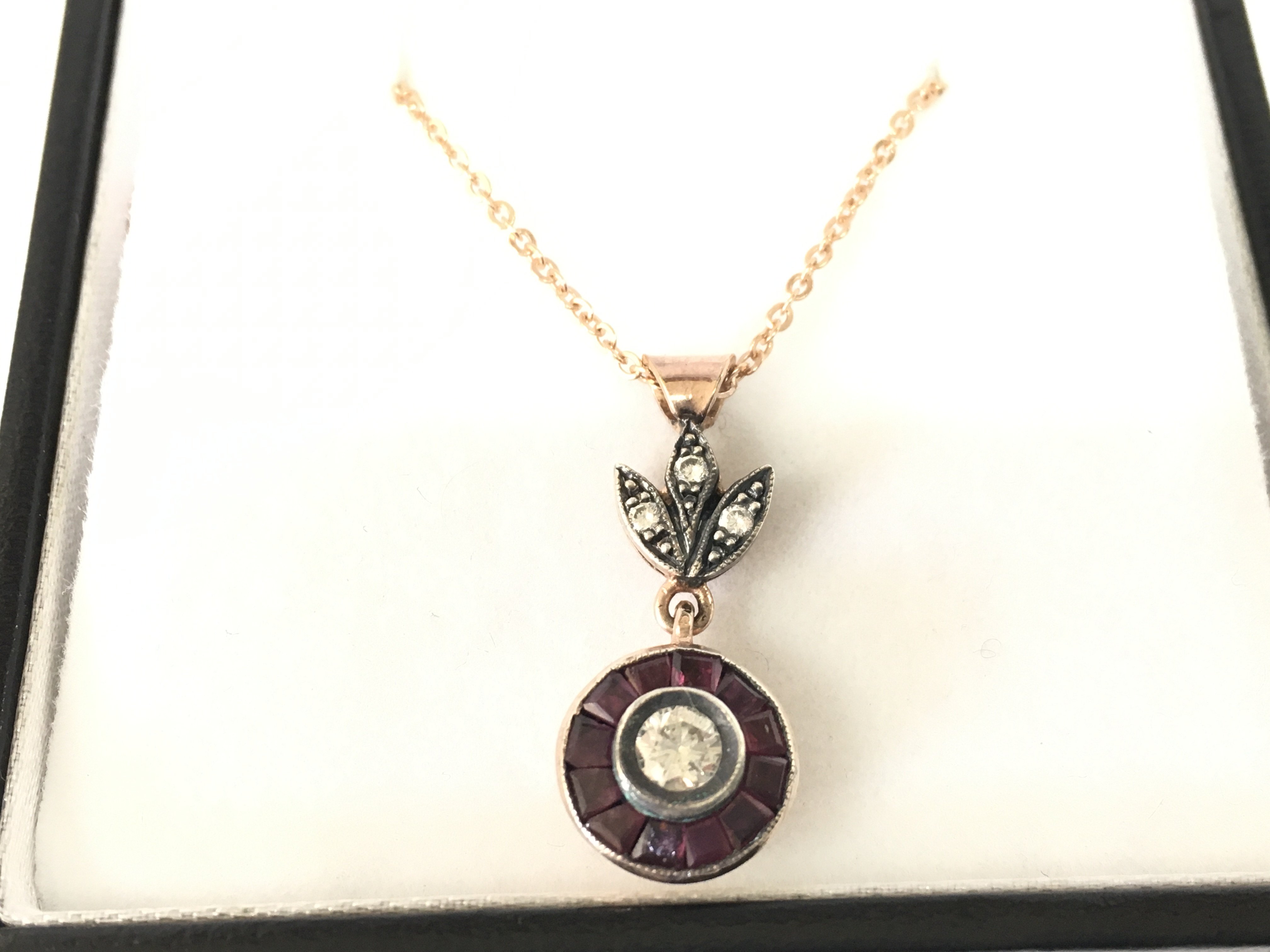 8ct rose gold target style pendant with floral bale set with RBC diamonds and calibre cut rubies on rose gold plated silver chain. Diamonds 0.30ct and Rubies 0.28ct approx.