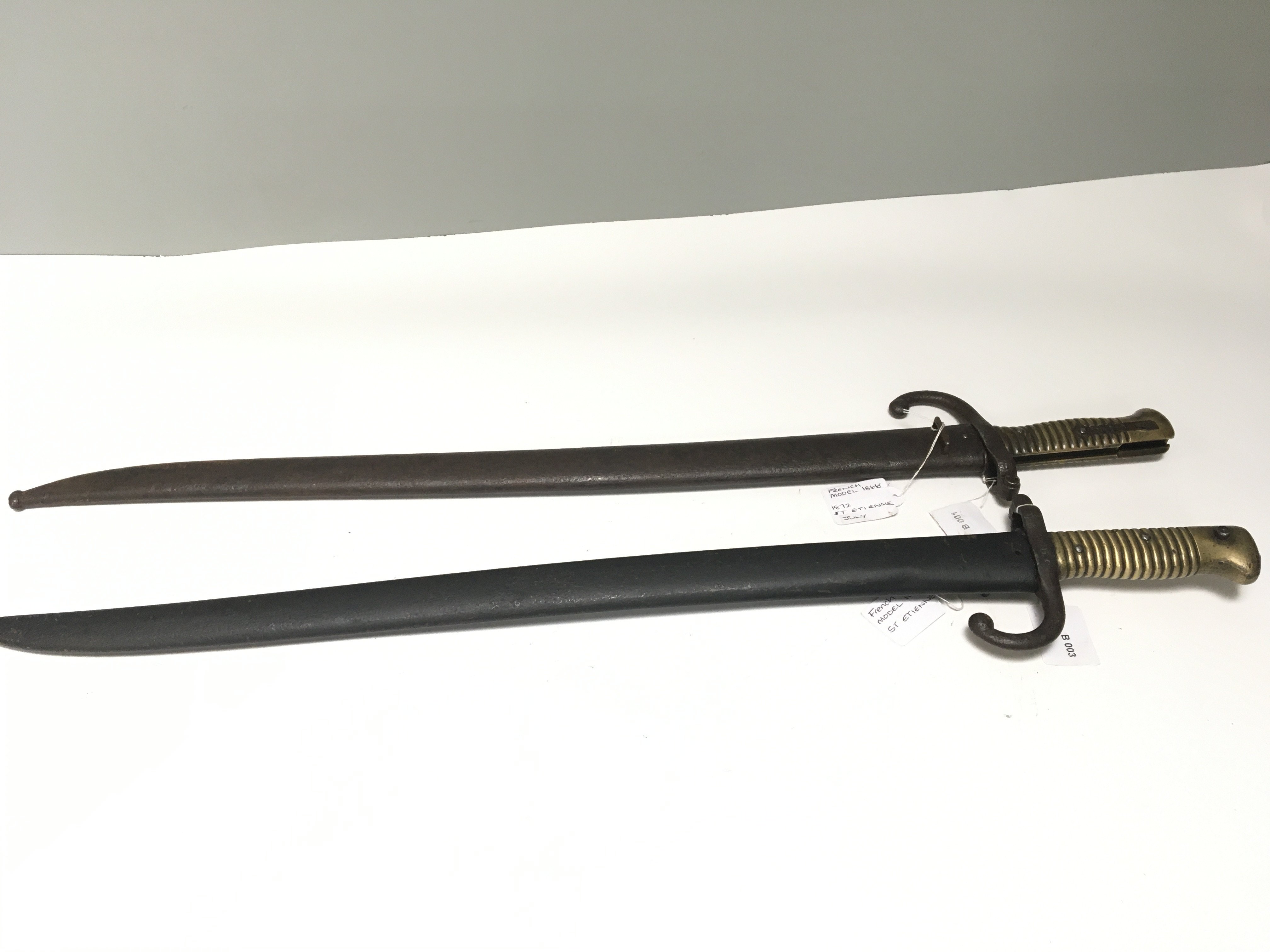 Two French bayonets the blade edge with inscriptions and dates both considered to be 1866 model bayonets with brass grips and steel scabbards (2)