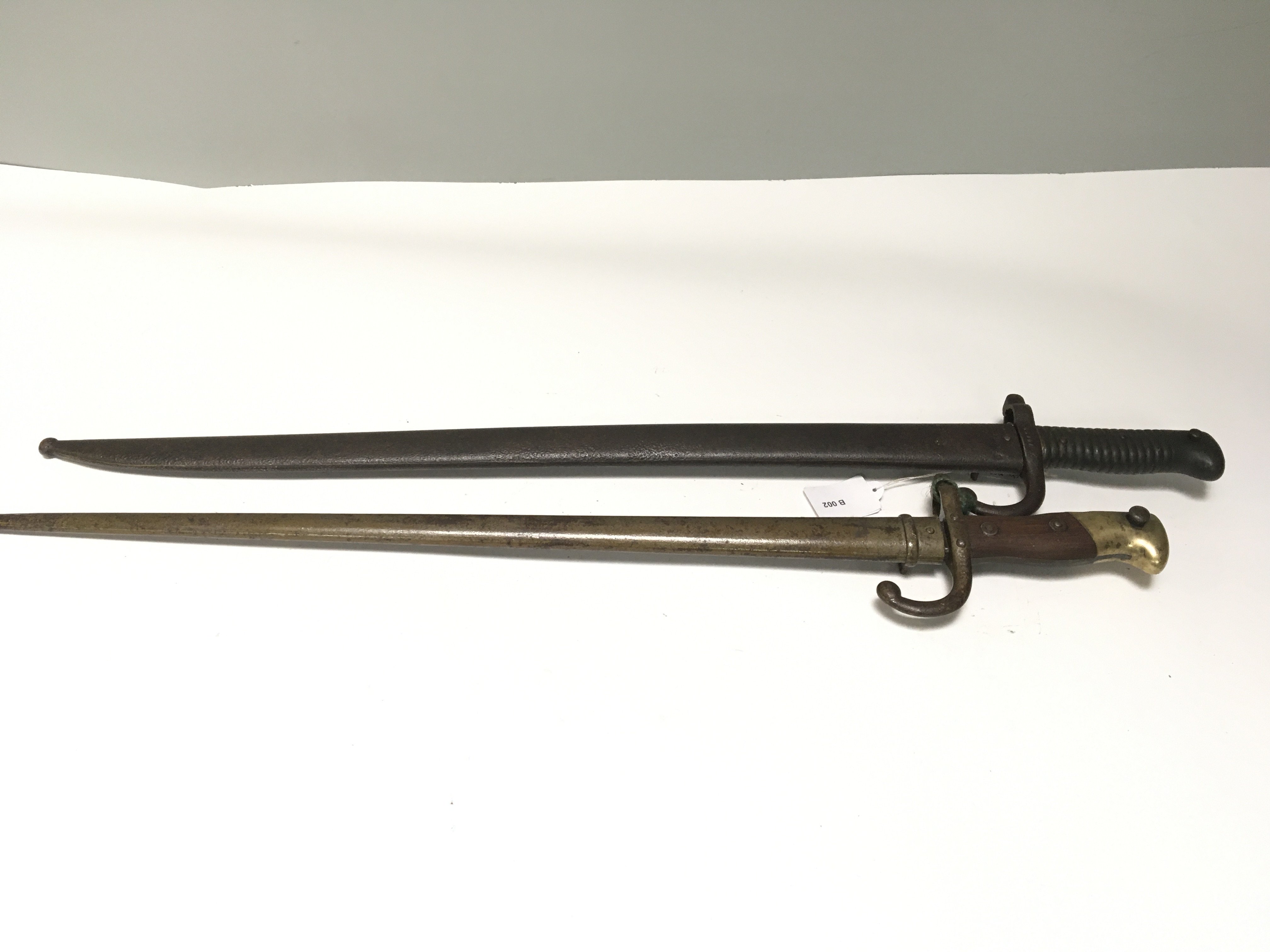 Two French bayonets an 1866 pattern with metal grip hook quilon and a later 1874 pattern with wood and brass grip both with metal scabbards. (2)