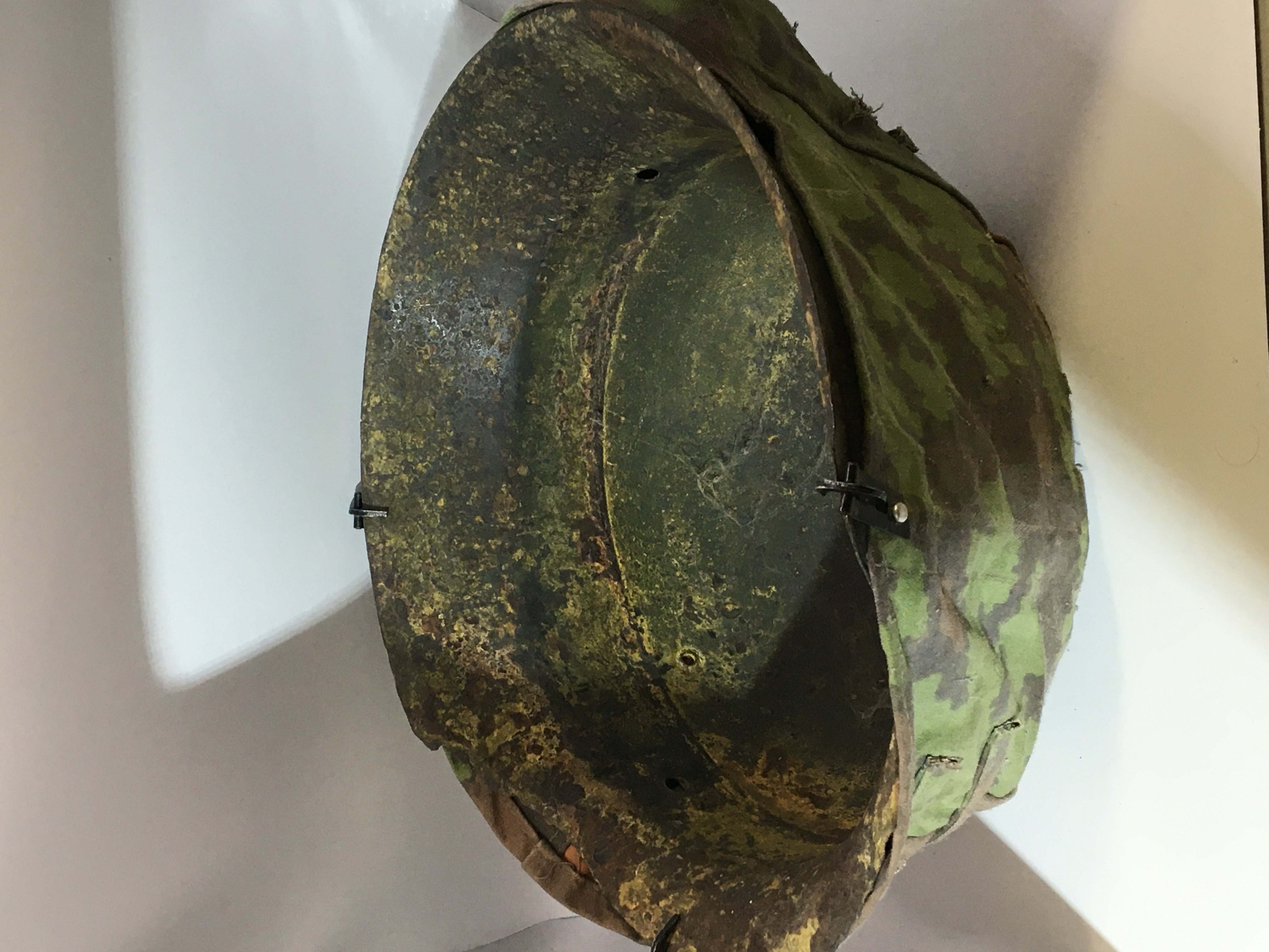 A German Third Reich II world war steel helmet M35 pattern with green camouflage double sided cover the helmet with no liner and areas of rust and wear particularly to the edges.