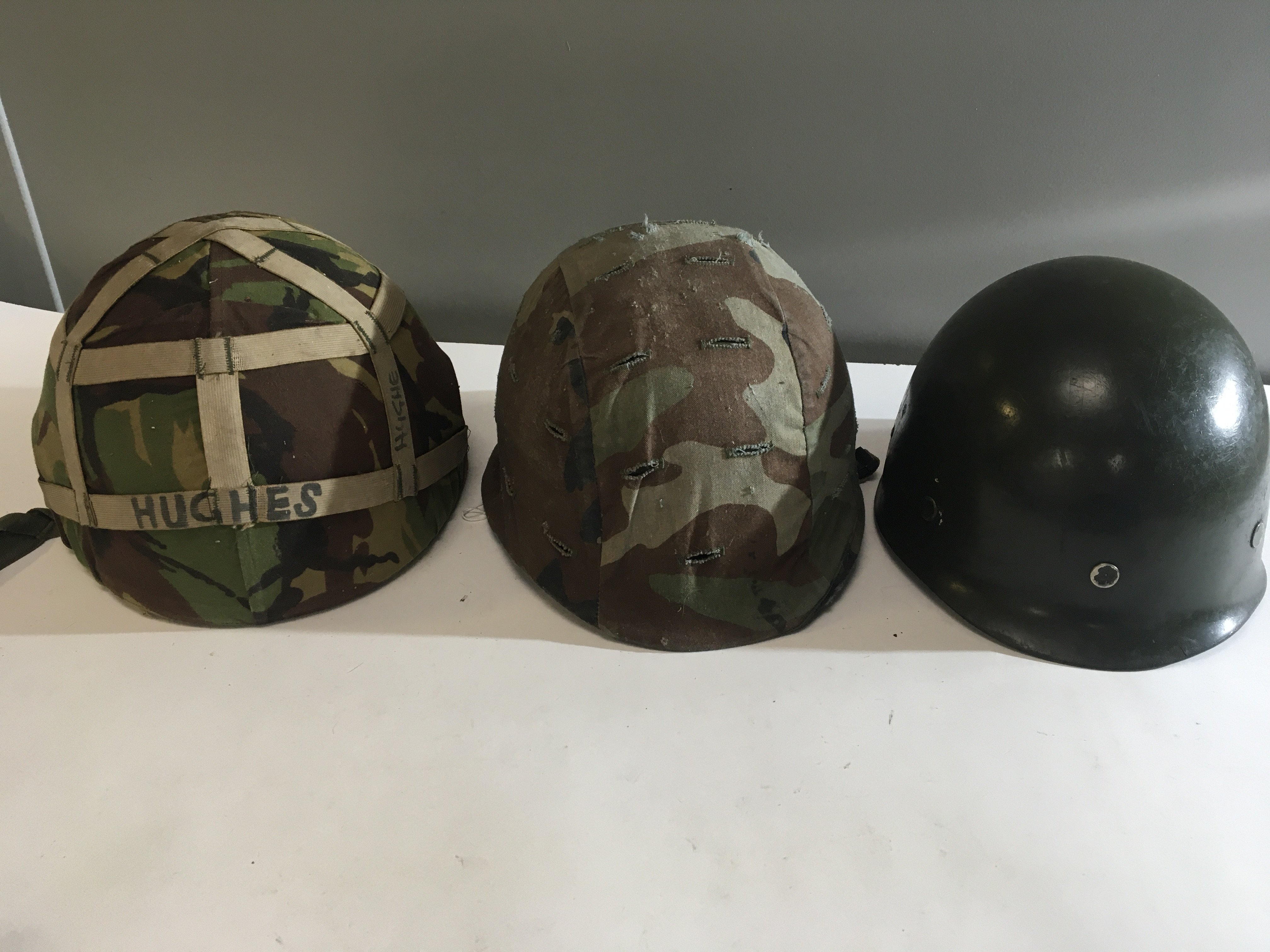 A British 1960 Military helmet with camouflage cover one other conforming helmet and a plastic helmet (3)
