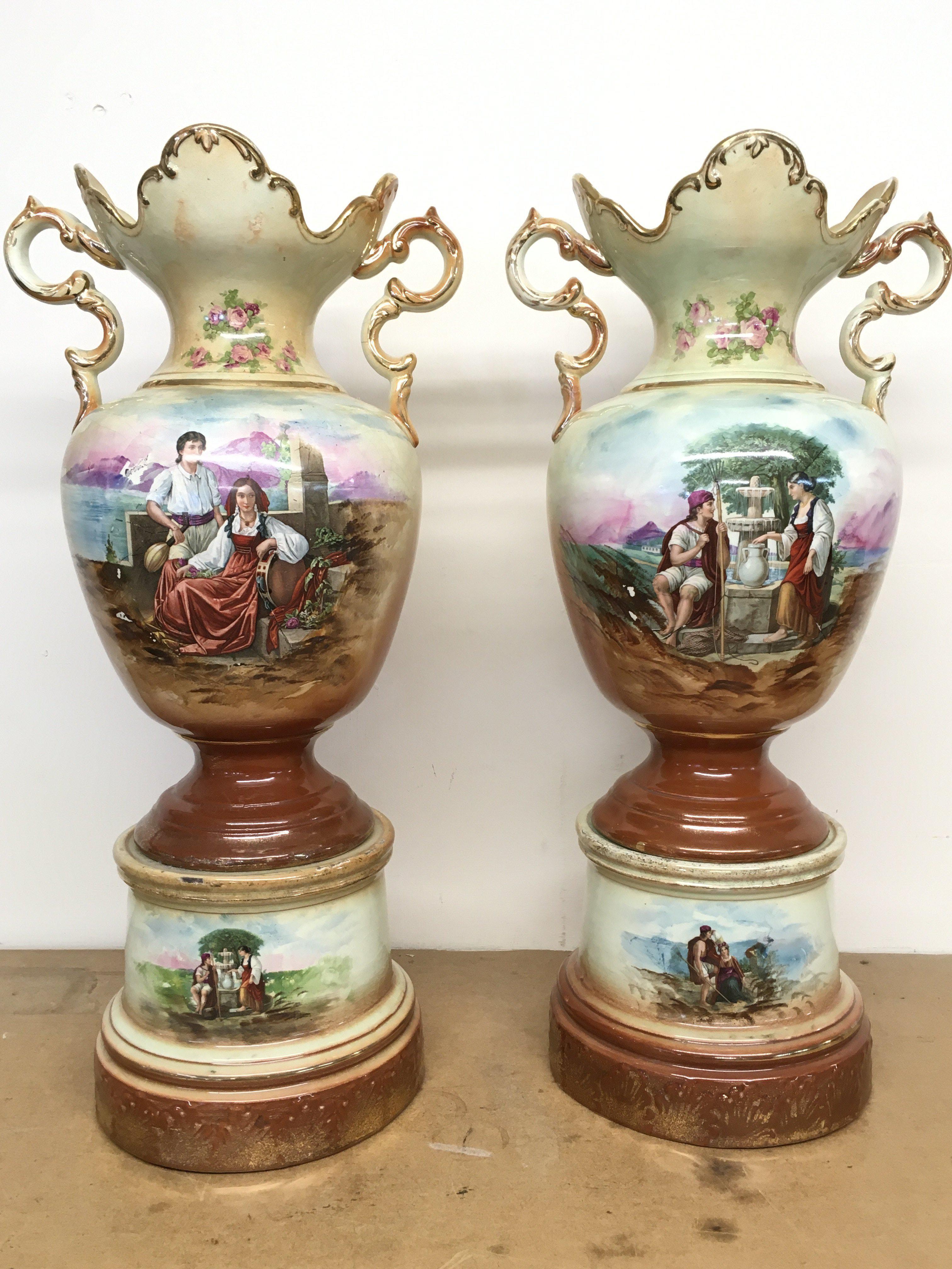 A pair of Victorian vases decorated with hand painted panels of classic scenes and pink rose designs , gilt detailing and handles, open tops and pedestal bases. 56cm tall approximate total height. This lot cannot be posted
