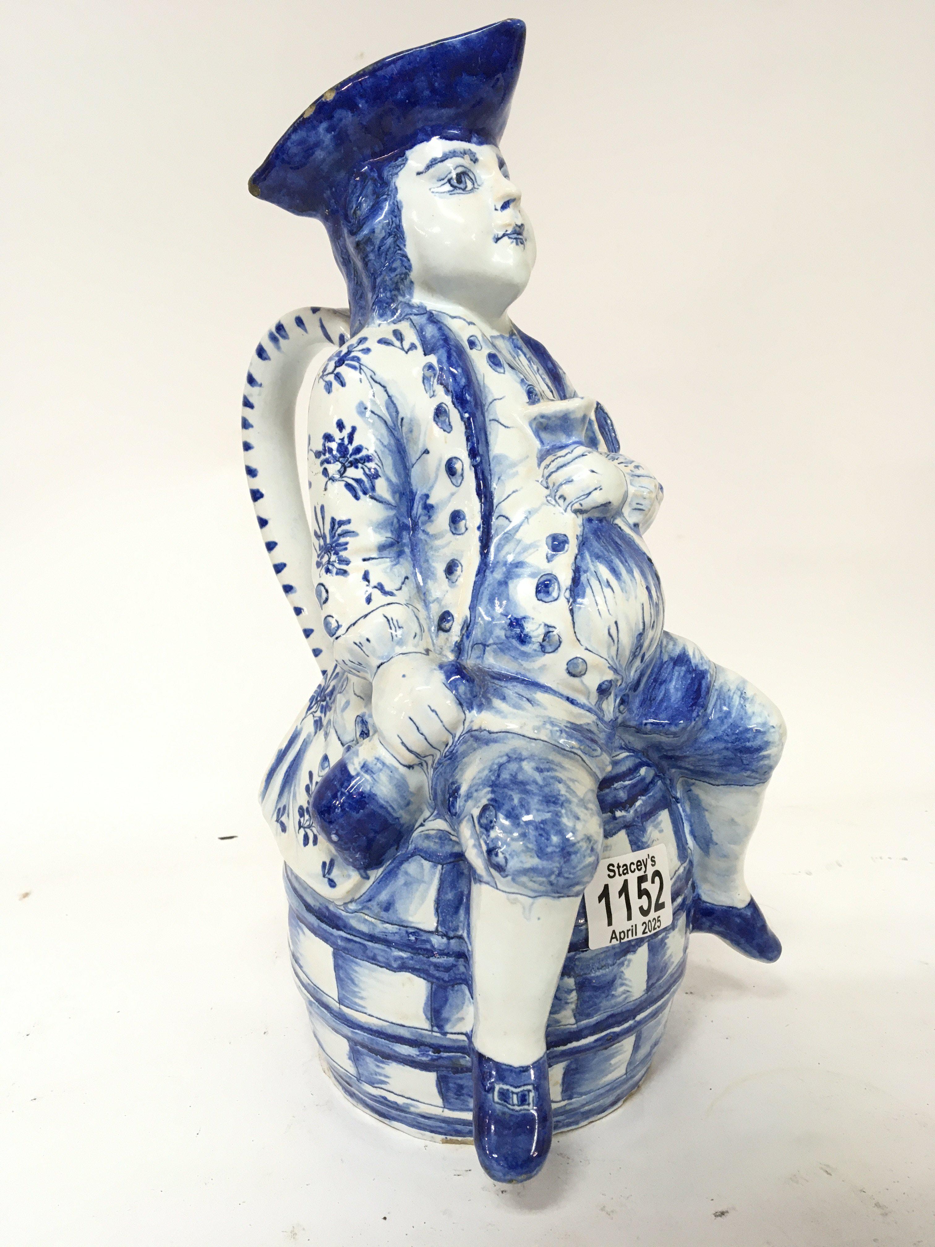 A Delft Character jug a figure with bottle and glass in hand sat on a barrel. Height 34cm makers marks to the base