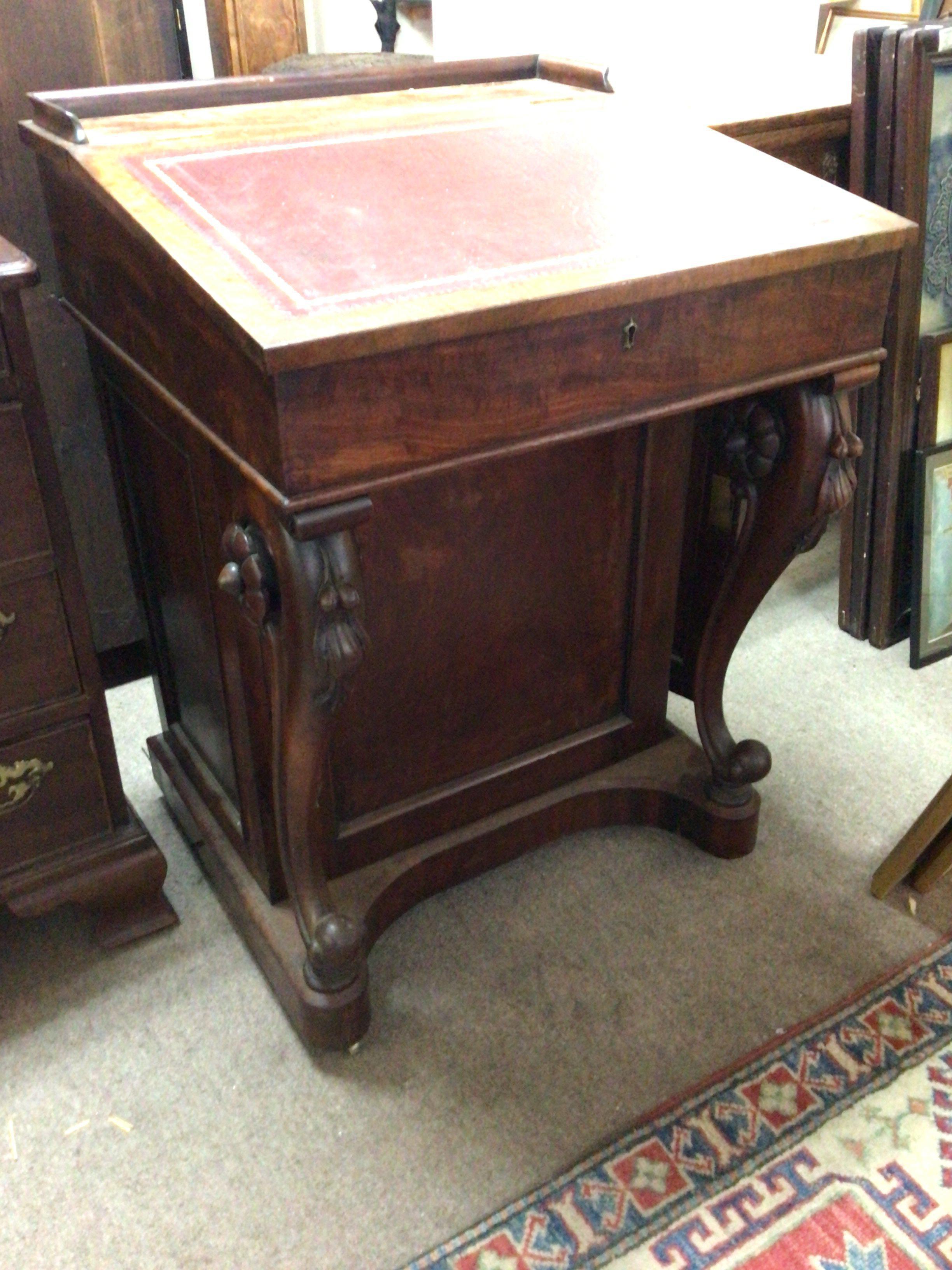 A William IV figured mahogany Davenport the hinged top enclosing a well fitted interior with satinwood drawers the scroll supports with raised floral roundels the side cupboard with a flight of four satinwood drawers.