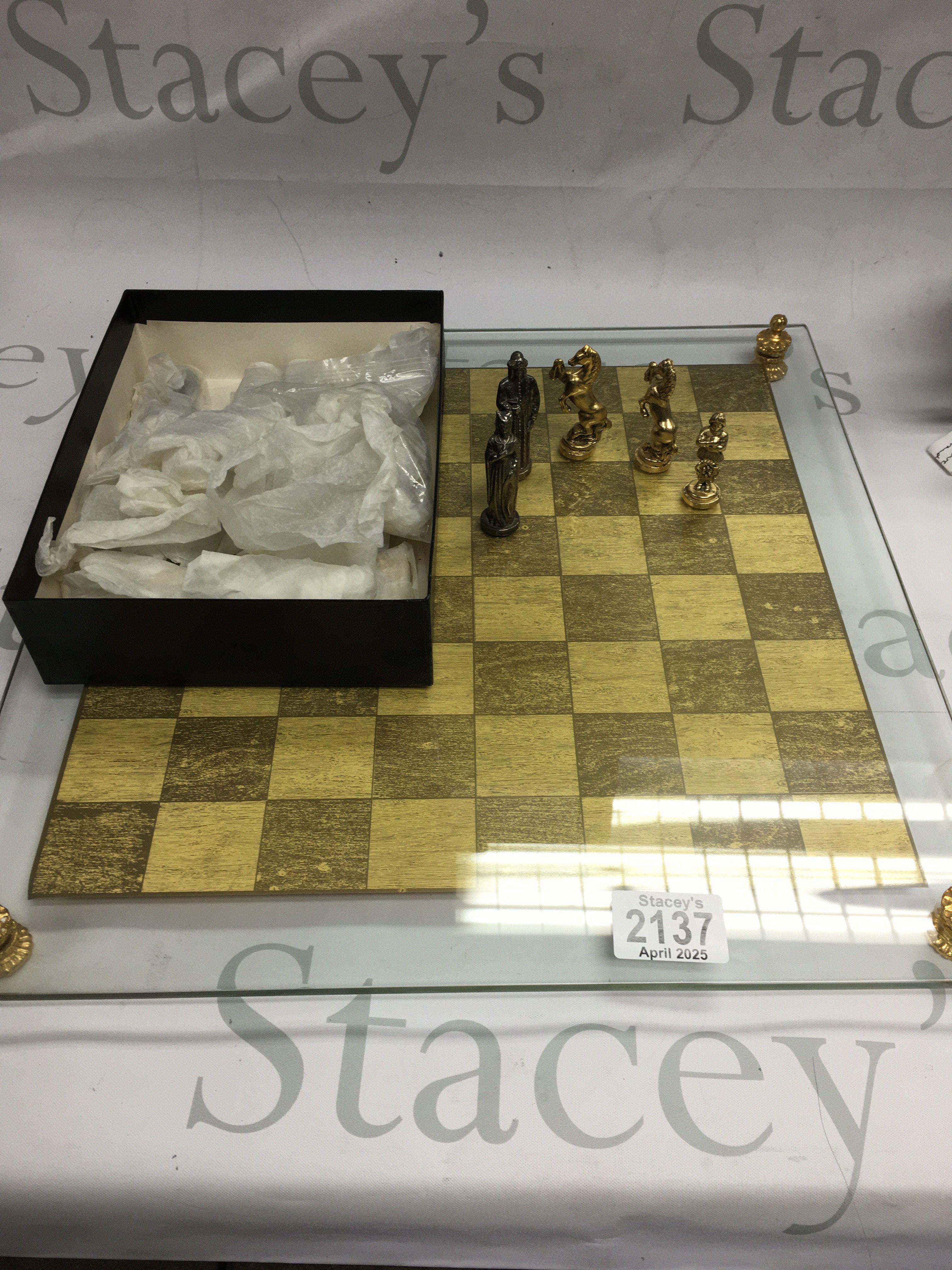 A glass chessboard with silver and gold coloured chess pieces.