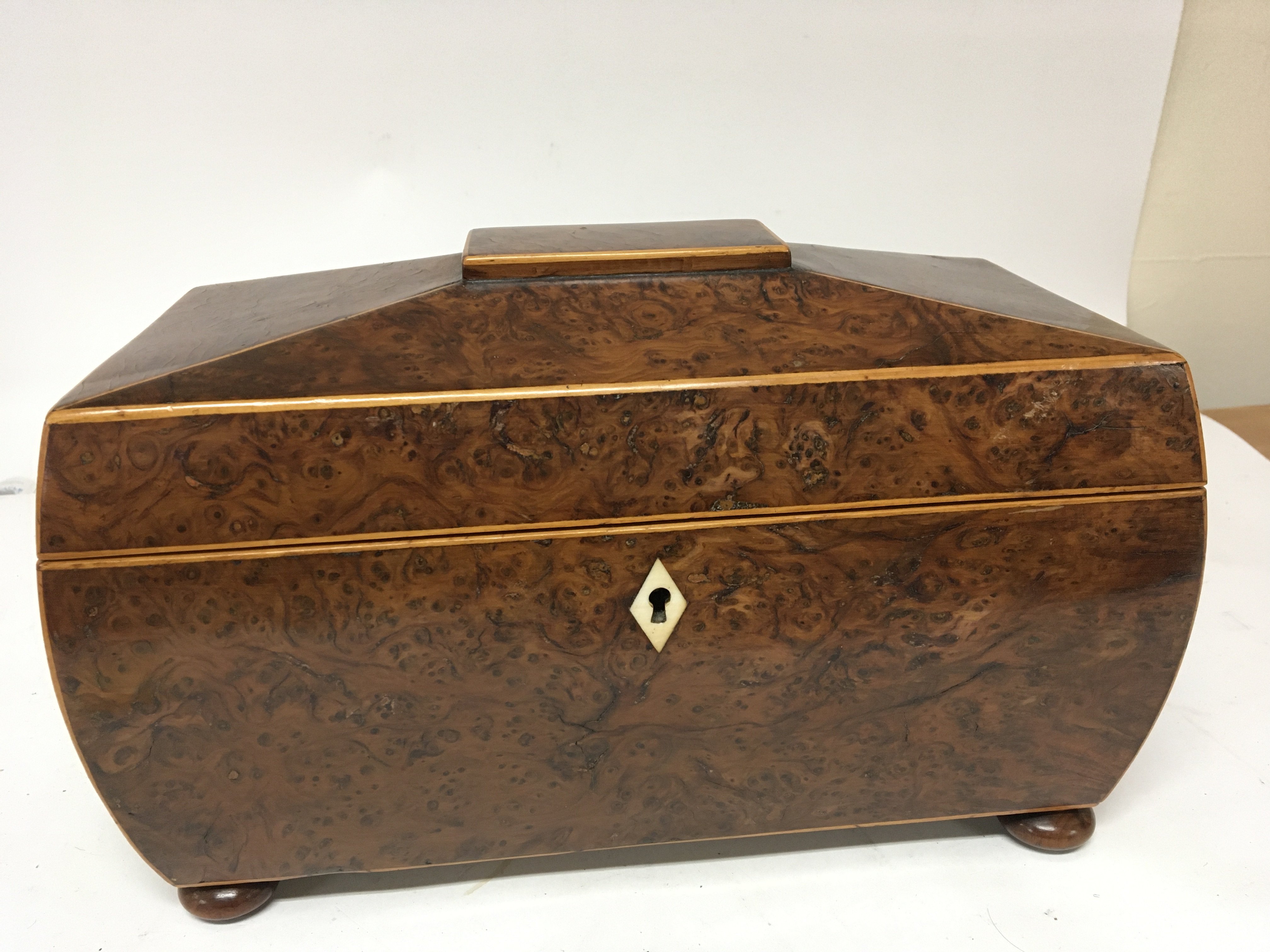 A burr walnut tea caddy with a shaped top and inverted sides with a well fitted interior with mixing bowl the sides with wooden ring handles. Length 35cm