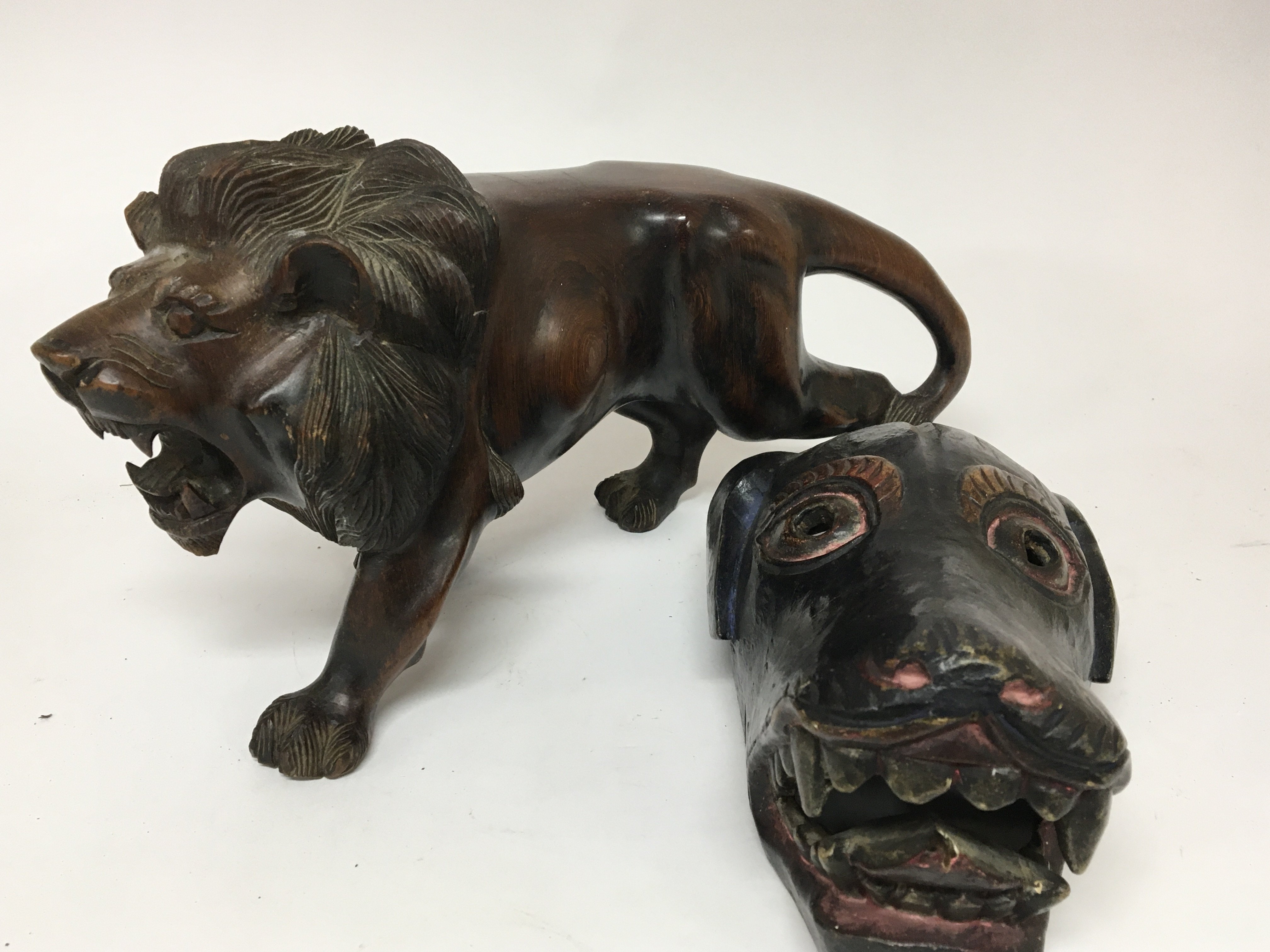 A carved hardwood sculpture of a lion length 40cm and a tribal art painted wood dog mask. (2)