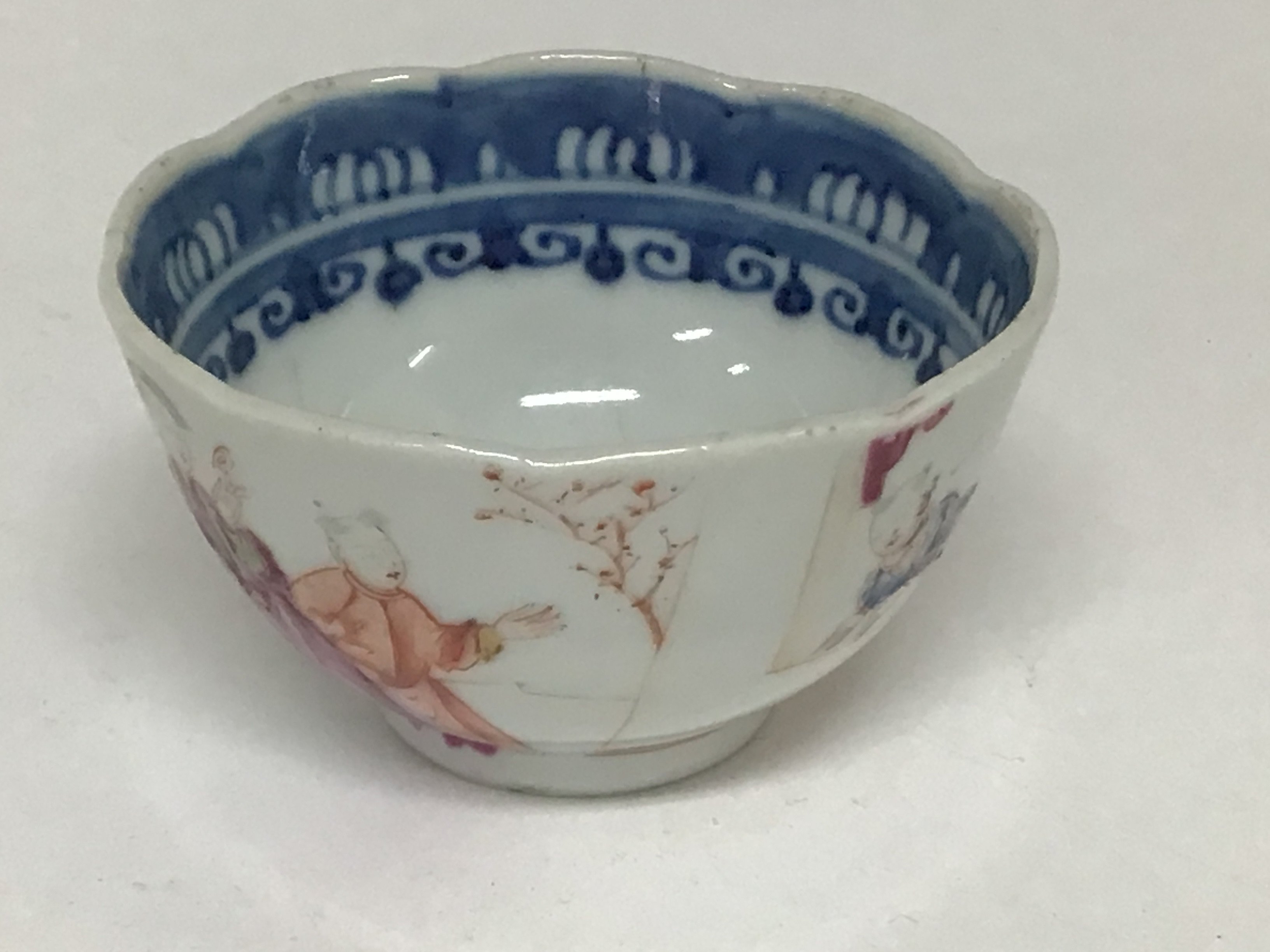 An 18th century Chinese Export porcelain tea bowl with a shaped edge the sides painted with figures in a windowed landscape. Slight hairline crack very minor chip to the rim. NO RESERVE