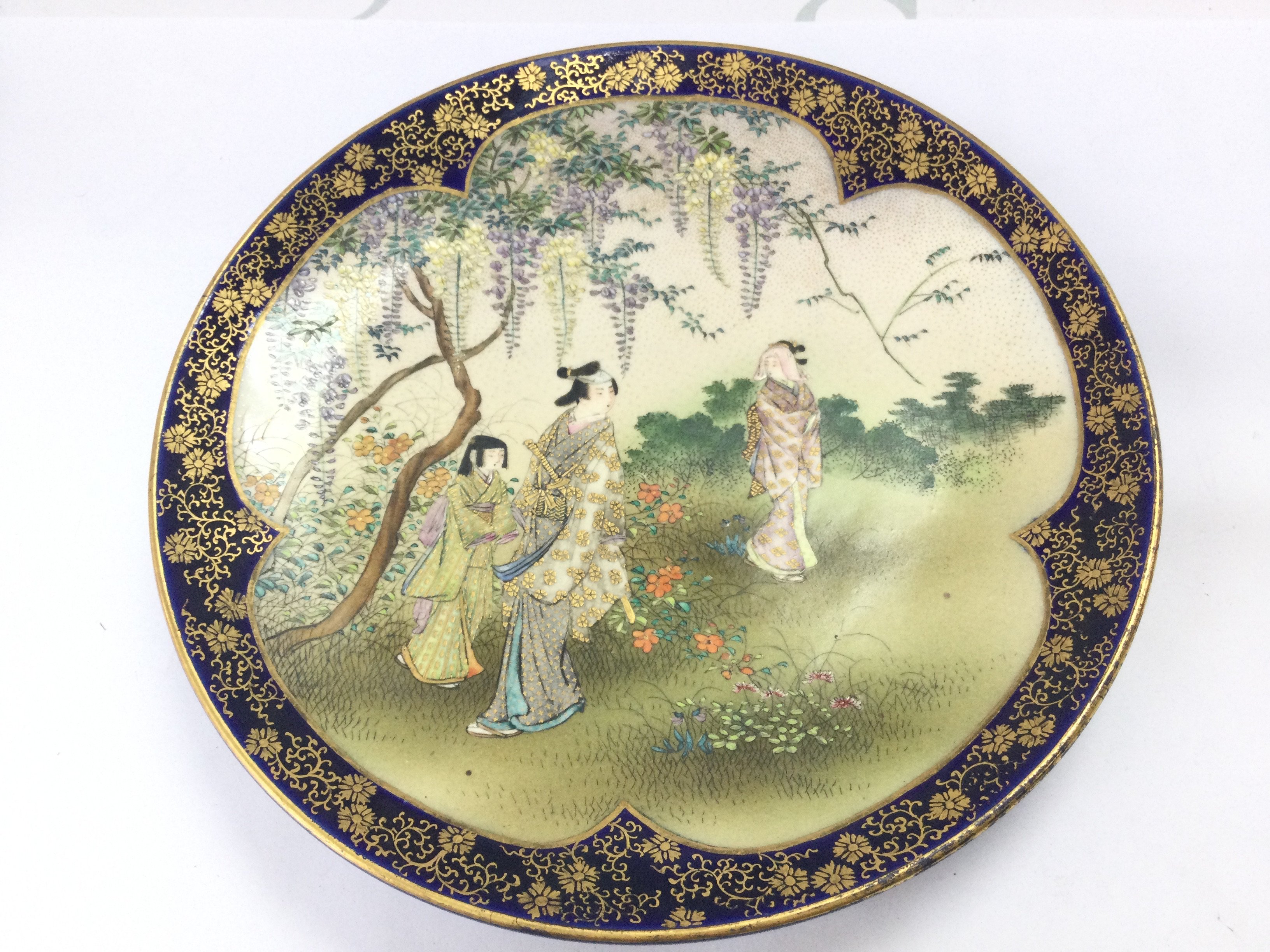 A Japanese Satsuma dish decorated with traditional figures in nature and a cobalt blue glaze underside. Dish 19cm wide