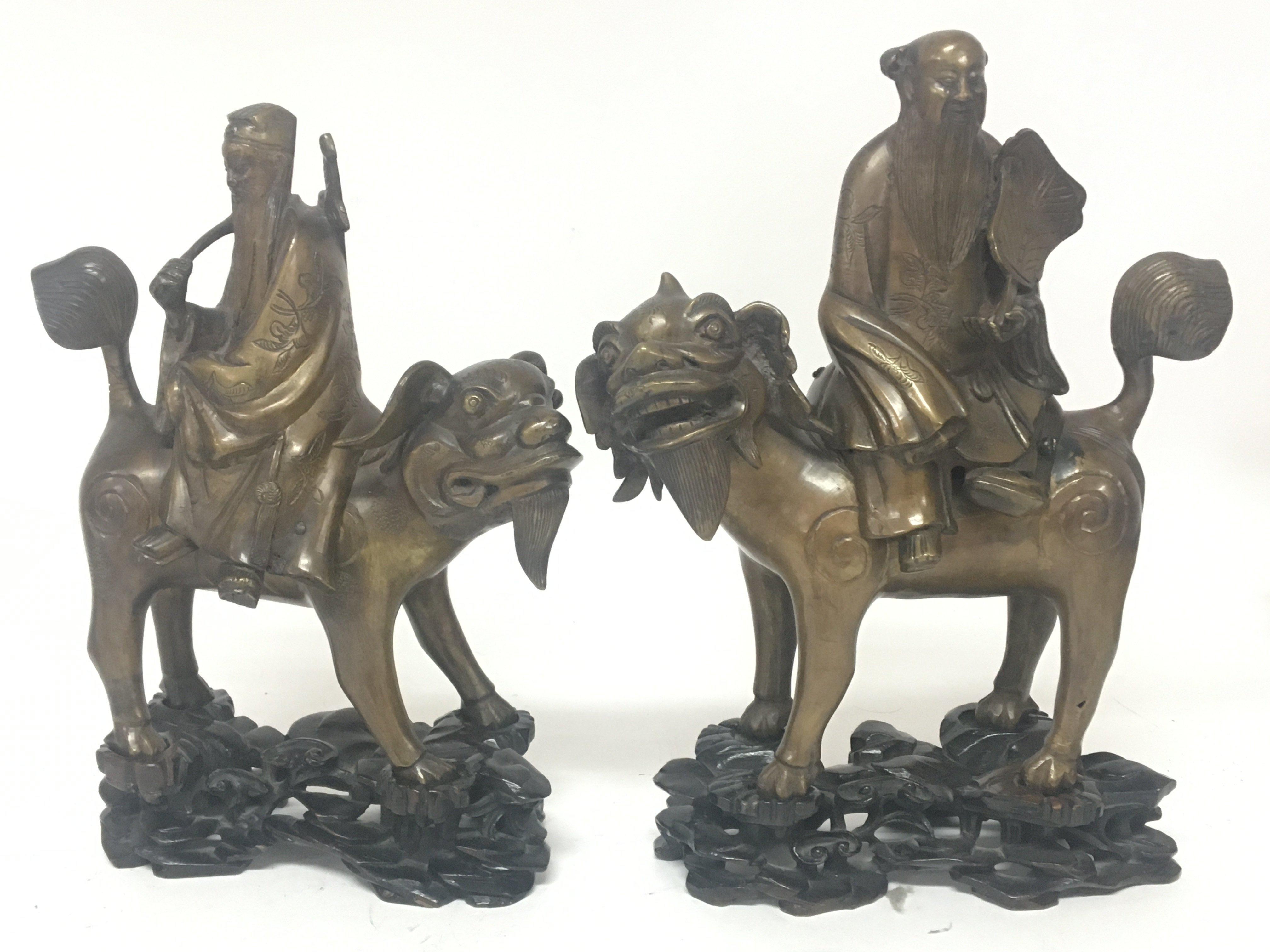 Two conforming 19th century Chinese bronze figures of seated elders on stylised temple dogs on carved hardwood stands height 30cm