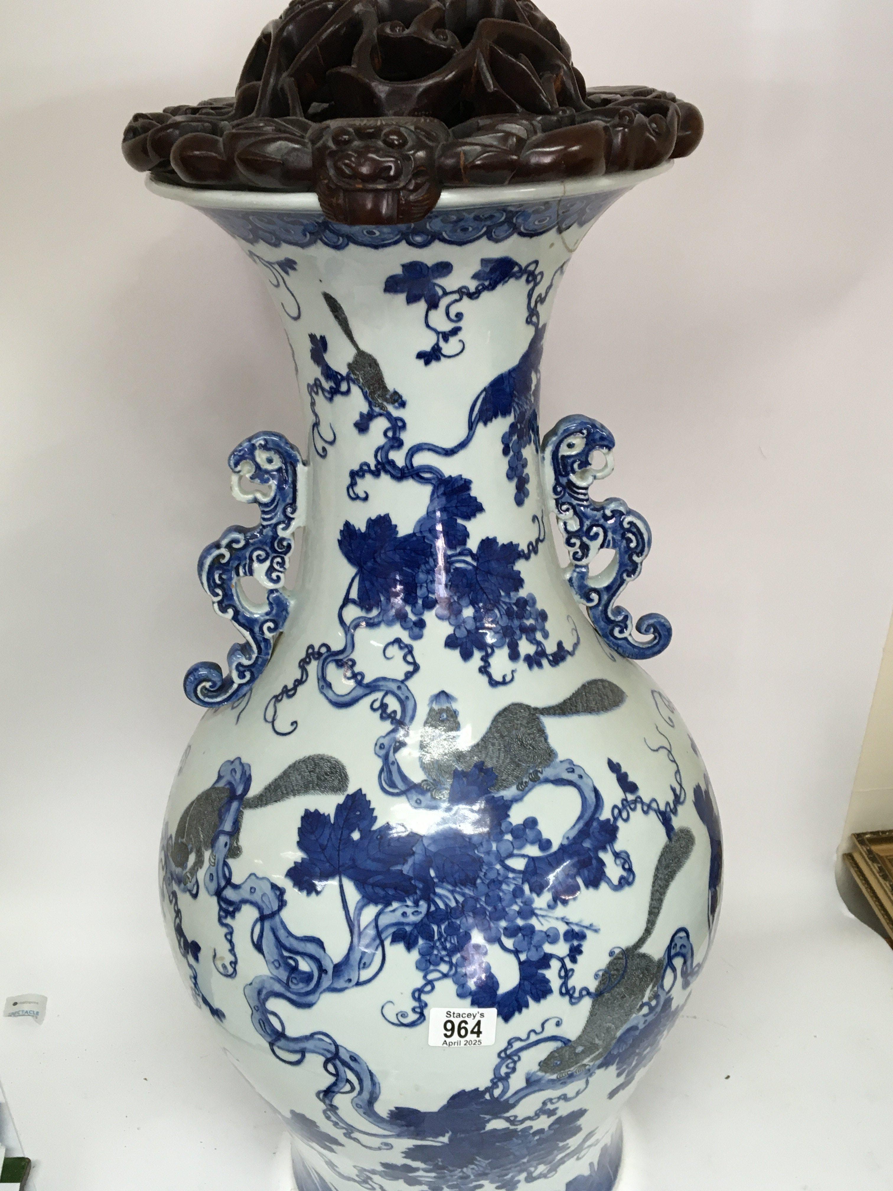 A large Chinese export porcelain blue and white floor vase decorated with animals amongst grape vines the sides with raised handles and the top with a carved wood cover some repair to the rim. 98cm high.