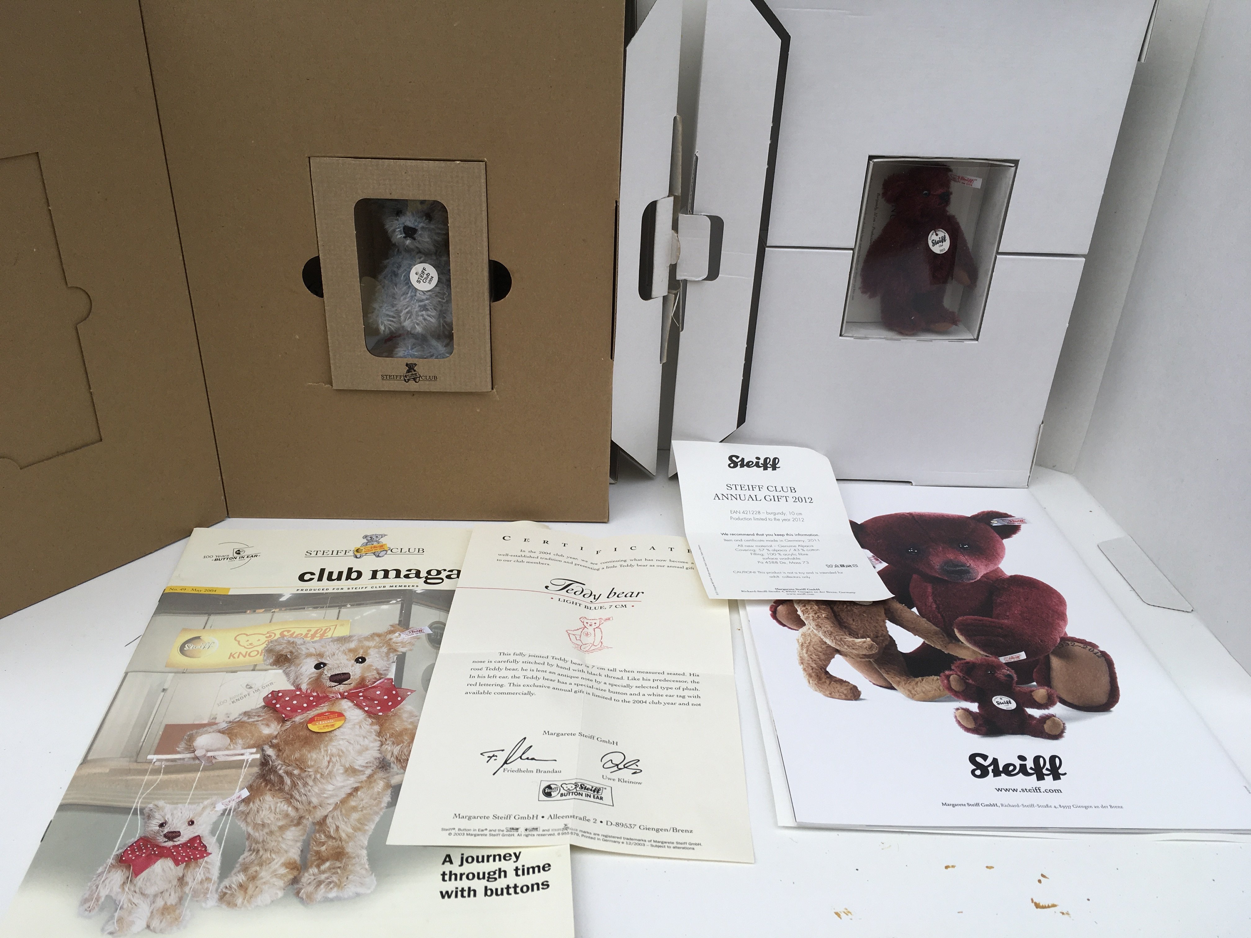 Two boxed Steiff minature teddy bears produced as annual gifts to Steiff Club members. Features a 2004 light blue 7pms and a 2012 burgundy 10pms complete with certificates and magazines. No Reserve (2)