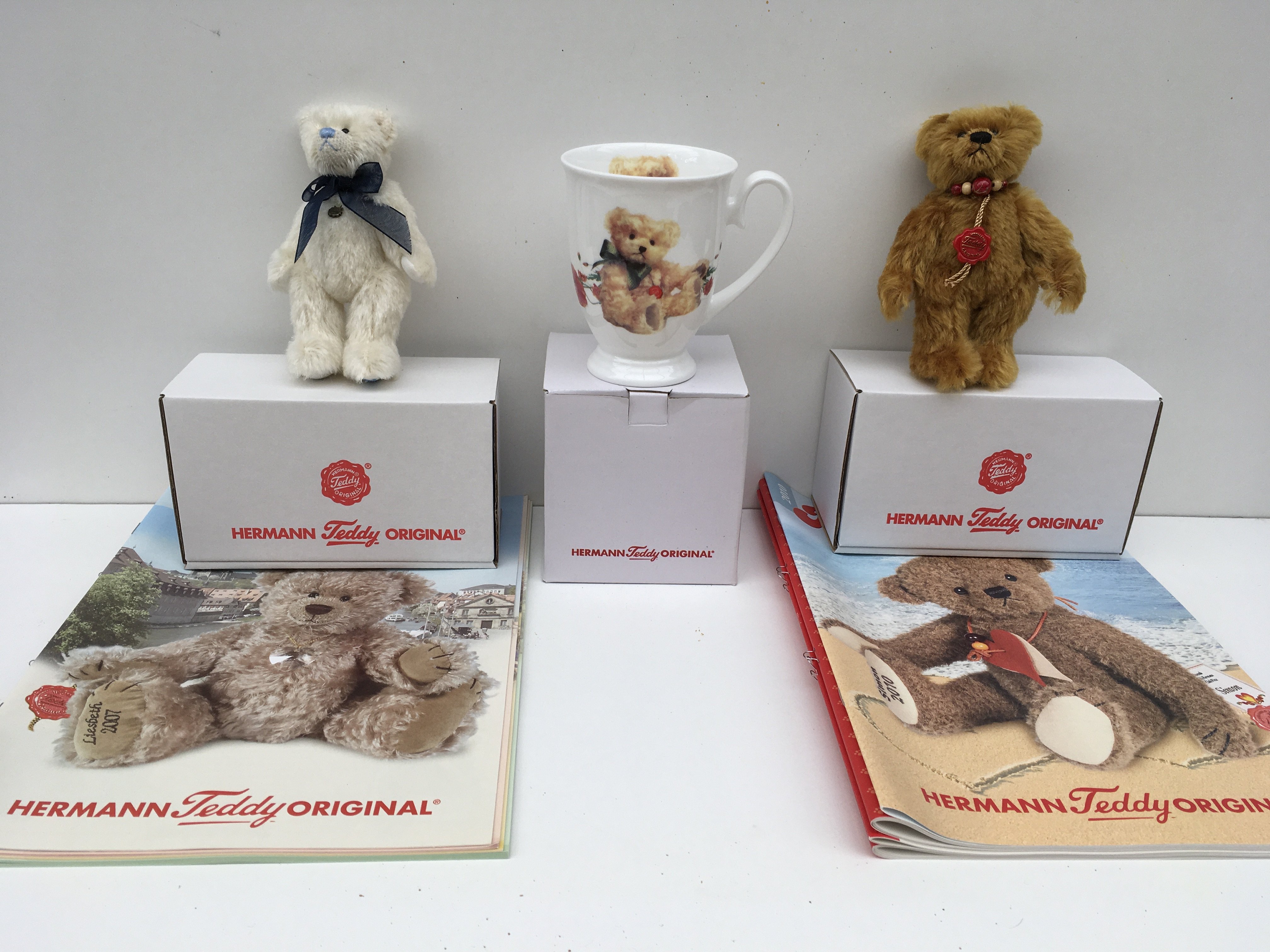 Two boxed minature Herman teddy bears from 2007 white and 2010 golden brown. Also includes a Herman&#2013266057۪s mug and some magazines. No reserve.