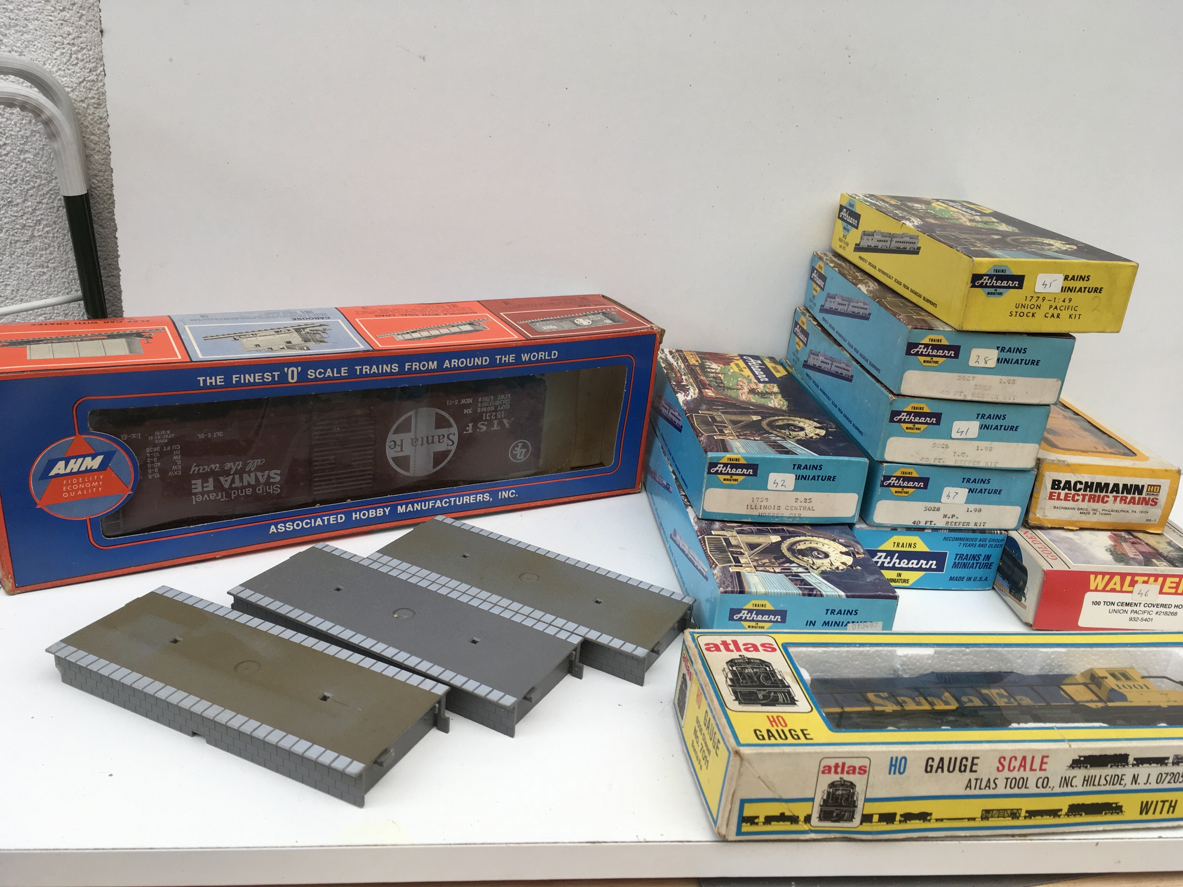 A collection of boxed HO gauge model railway items including 1x locomotive by Atlas and 9x assorted rolling stock by Athearn ..Bachmann and Walthers. Includes boxed O gauge Box Car by AHM and 3x platform sections. No reserve
