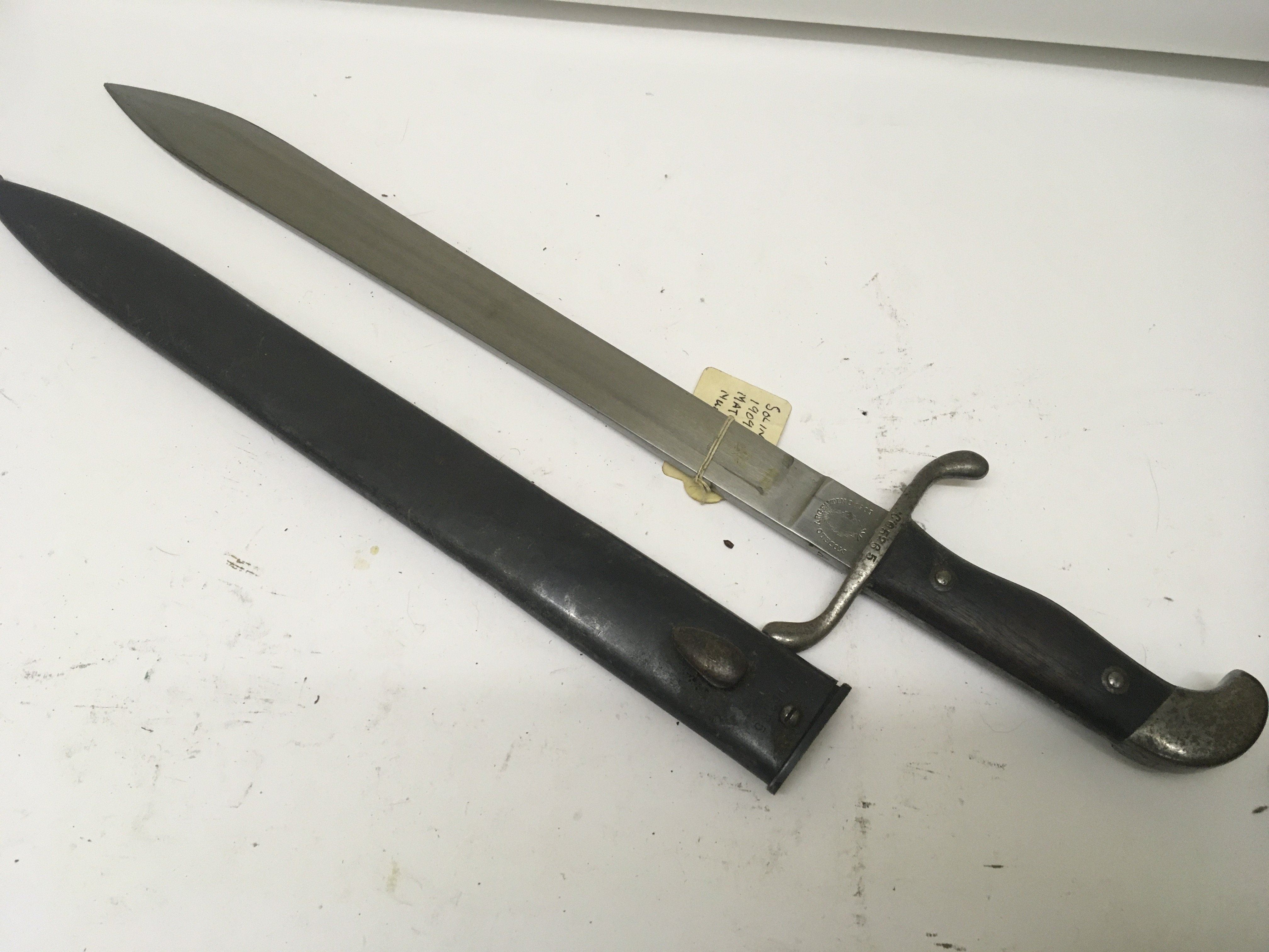 A Short Sword with butcher type steel blade wood grip the blade stamped Modelo Argentino 1909 the cross guard and scabbard with conforming serial number and in very good condition. length 51cm